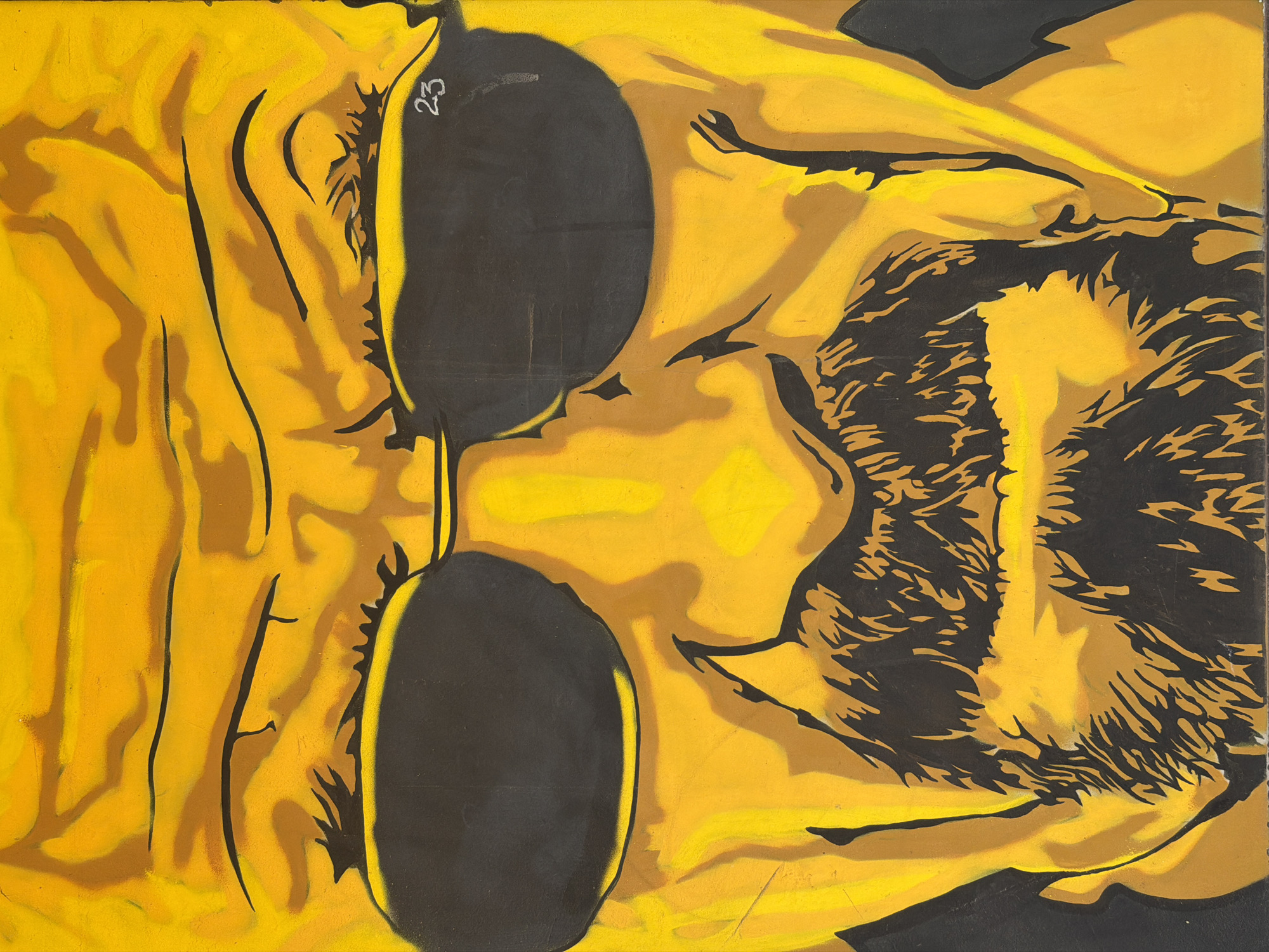The image is a close-up, stylized portrait of a man's face, rendered in shades of yellow and black. The man wears dark sunglasses and has a beard and mustache. The background is a solid yellow with black outlines and shading that suggest wrinkles on the forehead and around the eyes. The overall impression is one of a graphic novel or stencil art style. There is a small detail of the number "23" written in white on the right lens of the sunglasses. The image does not contain any information about a specific location in a city.