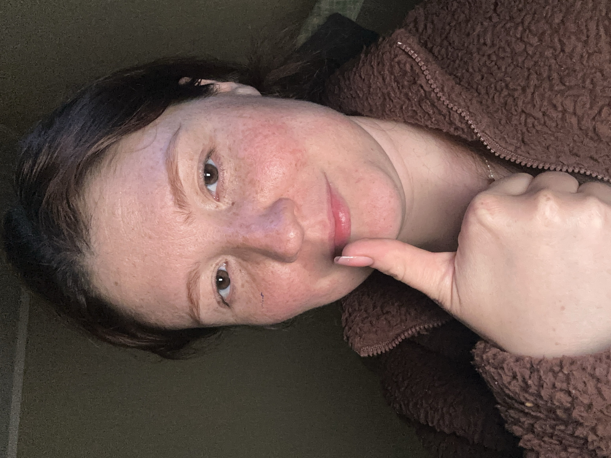 A person with brown hair and fair skin is shown wearing a brown, textured jacket. The person's thumb is extended and pointed upwards towards their face, in an ambiguous gesture. There is no indication of the location being Nizhny Novgorod, Russia, or any specific identifiable environment.