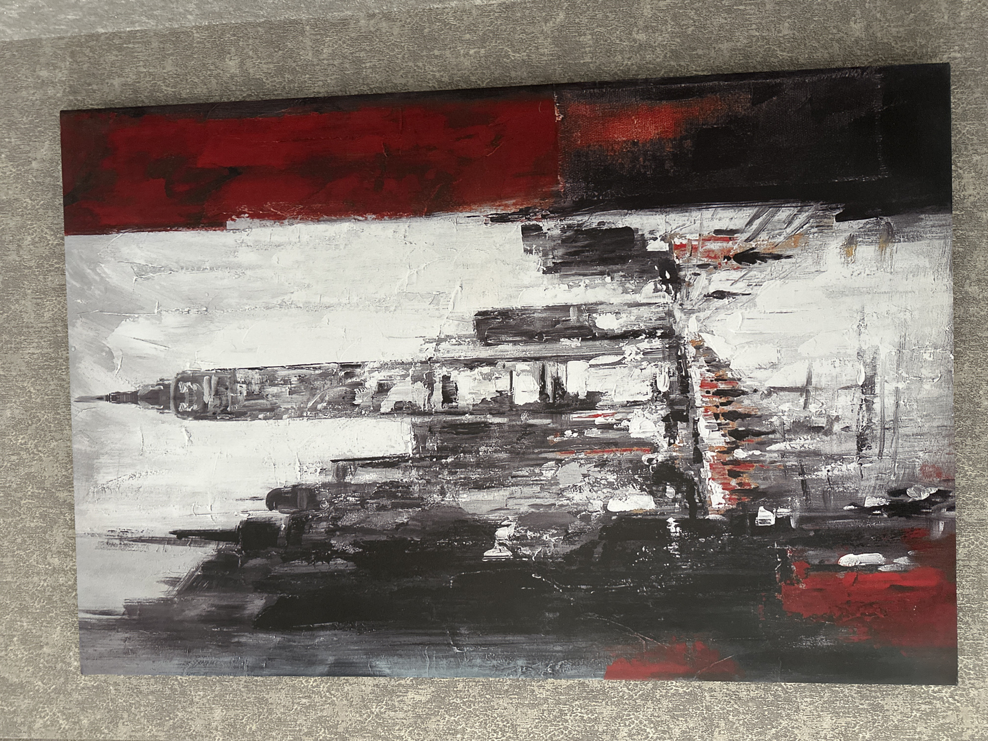 This is an abstract painting of a city street scene. The dominant colors are black, white, and red, with some gray and hints of orange. The painting depicts tall buildings, suggestive of a city skyline, with a street in the foreground. There are small, silhouetted figures walking on the street, some with umbrellas, suggesting a rainy or overcast day. The style is impressionistic, with thick brushstrokes creating texture and a sense of movement. The red element on the right side of the painting appears as a large vertical band, possibly representing a building or a strong visual accent. There is no discernible evidence in the painting that indicates the location is Minsk, Belarus.