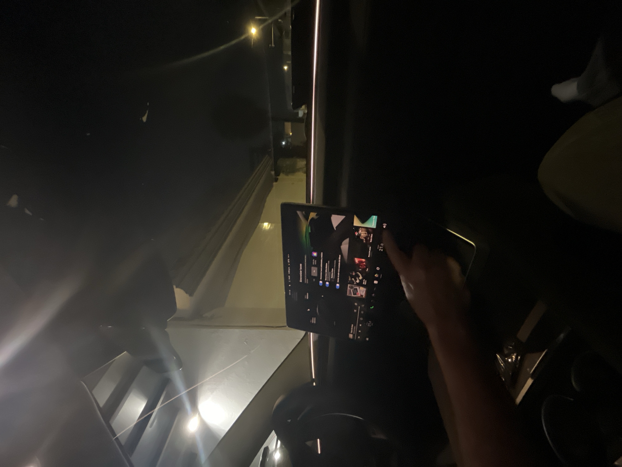 The image appears to be taken inside a vehicle at night. A touchscreen display, likely a car infotainment system, is visible. A person's hand is interacting with the screen. The background shows glimpses of an urban environment with street lights and buildings, possibly aligning with the city of San Bernardino Tlaxcalancingo, Mexico.