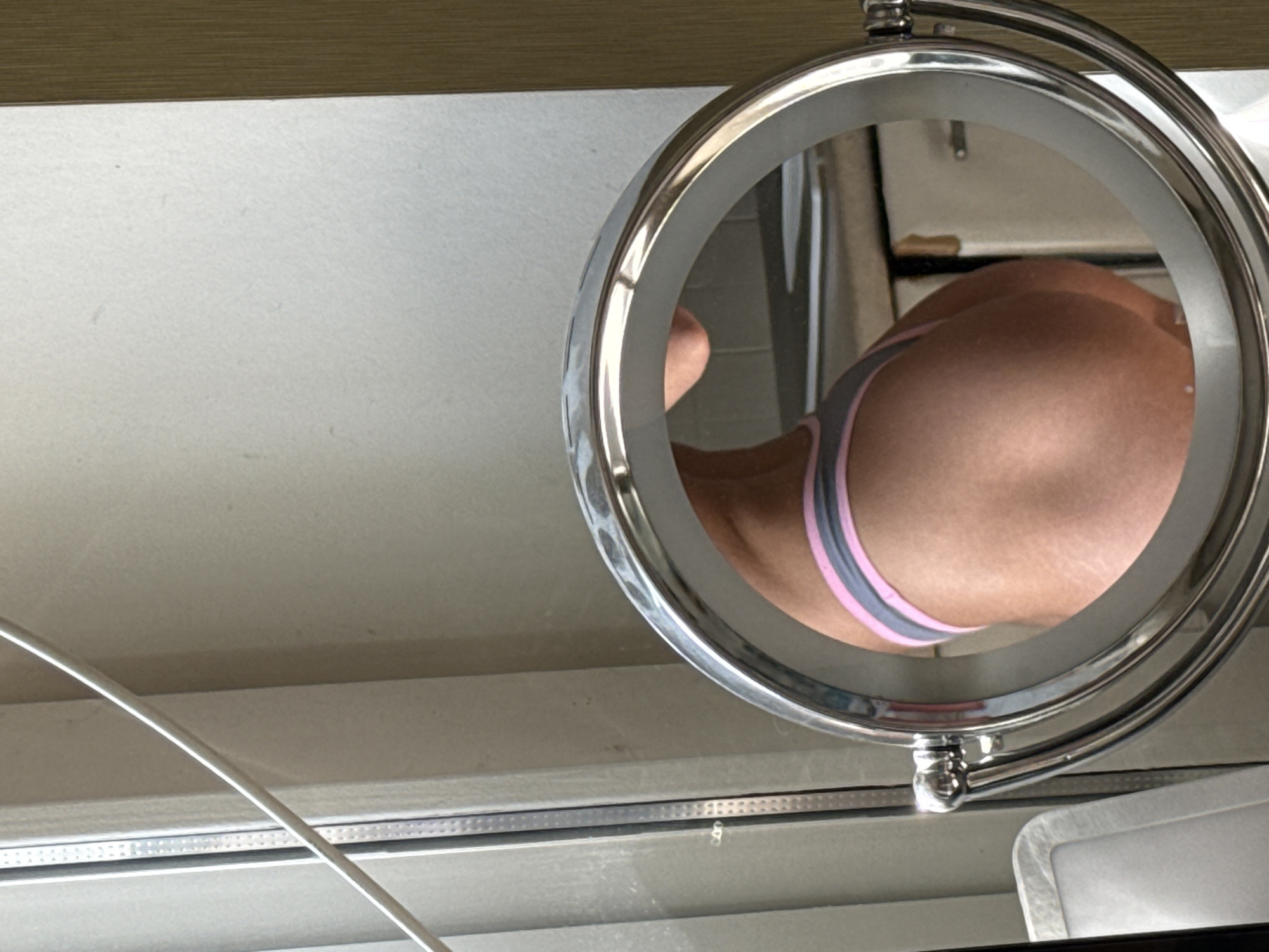 The image shows a close-up of a vanity mirror reflecting a person's buttocks wearing underwear with a grey and pink band. The environment appears to be a bathroom or dressing area, based on the mirror and counter surface. There is a white cord or cable visible on the left side of the image. The location in Saint Petersburg, Russia, is not discernible from the information in the image.