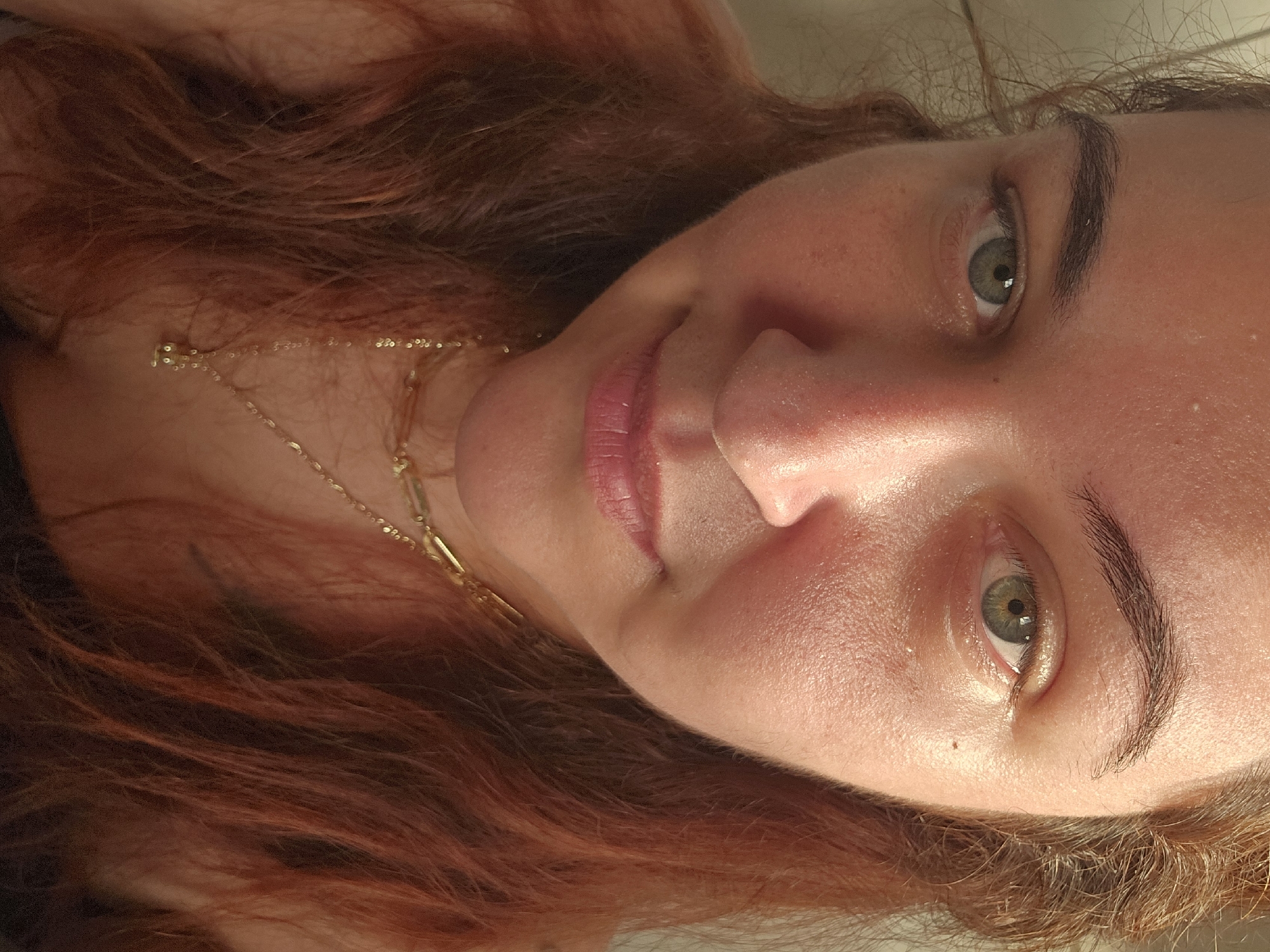 A close-up portrait of a woman with red hair, light skin, and green eyes, wearing a gold necklace. The photograph is taken at an angle, with the woman's face tilted towards the camera. There is no verifiable information in the image to indicate a location in Zirndorf, Germany.