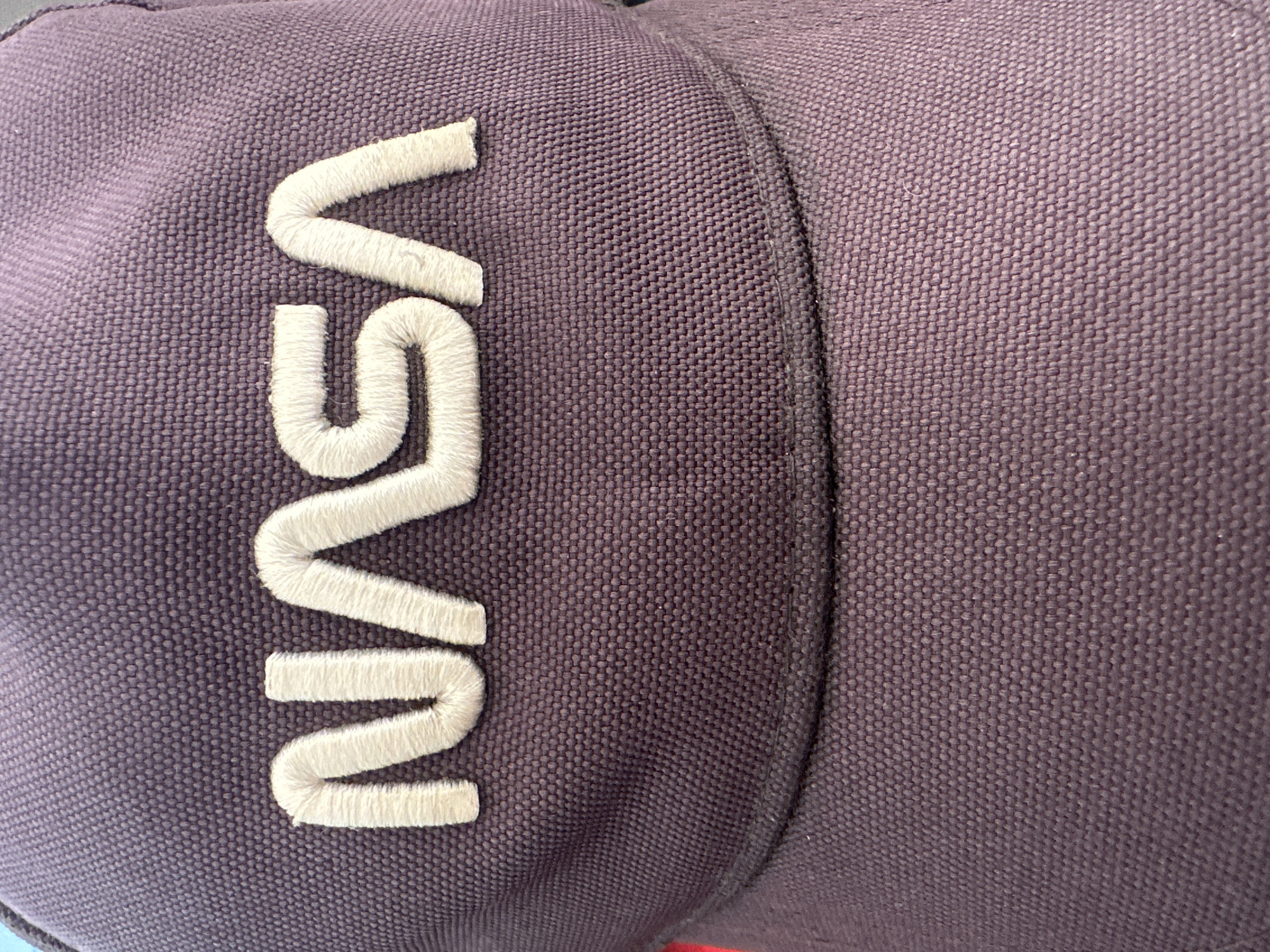 The image shows a close-up of a dark purple baseball cap with "NASA" embroidered in white thread on the front. The embroidery is raised and textured. The fabric of the cap has a visible woven pattern. The background is out of focus and appears to be the same dark purple fabric of the cap. There is no information in the image to indicate its location in Łódź, Poland, or any other city.