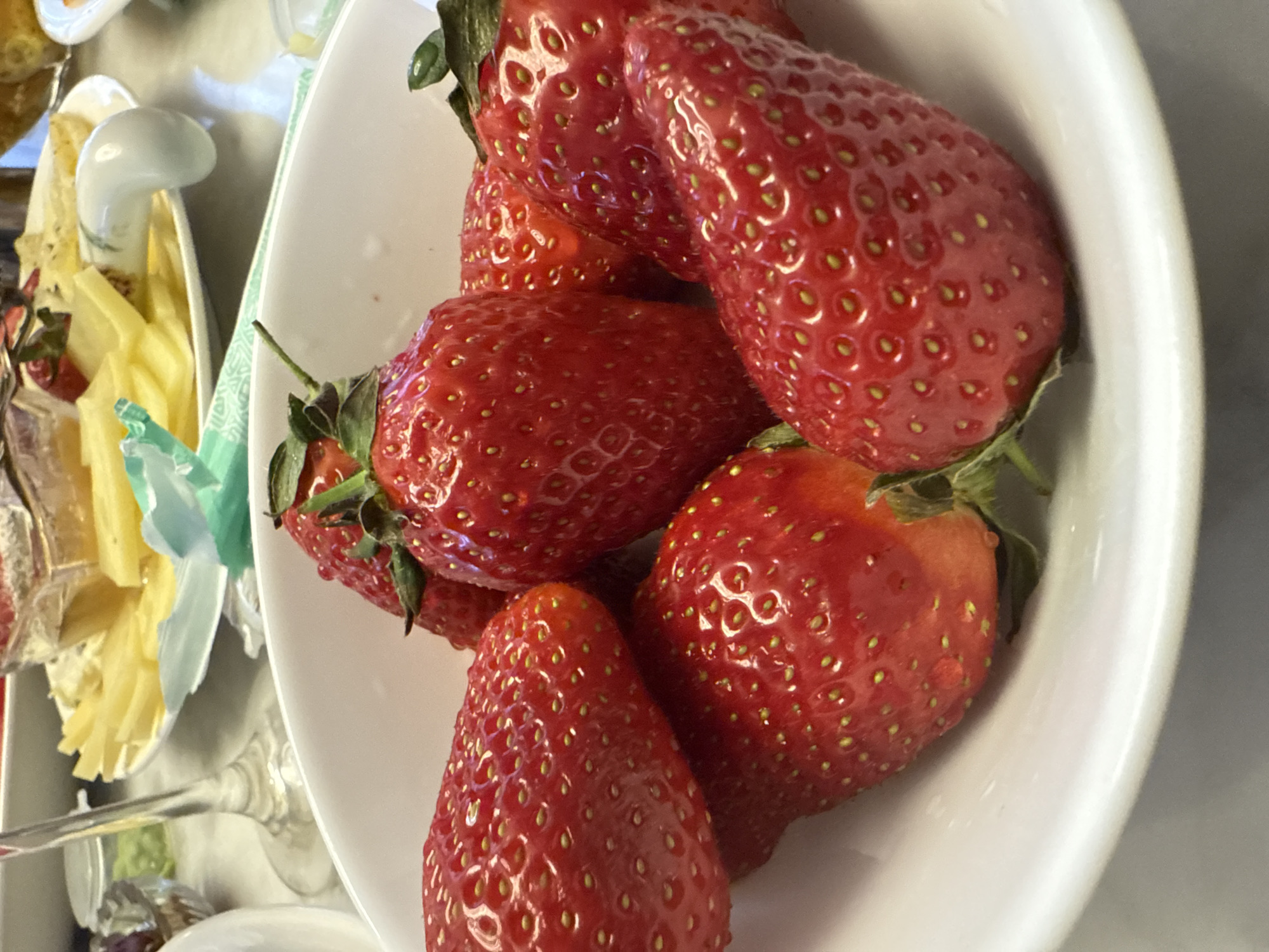 A white bowl contains several ripe red strawberries. To the left of the bowl is another plate with cheese. The scene appears to be indoors. There is no evidence indicating the city of Saint Petersburg, Russia.