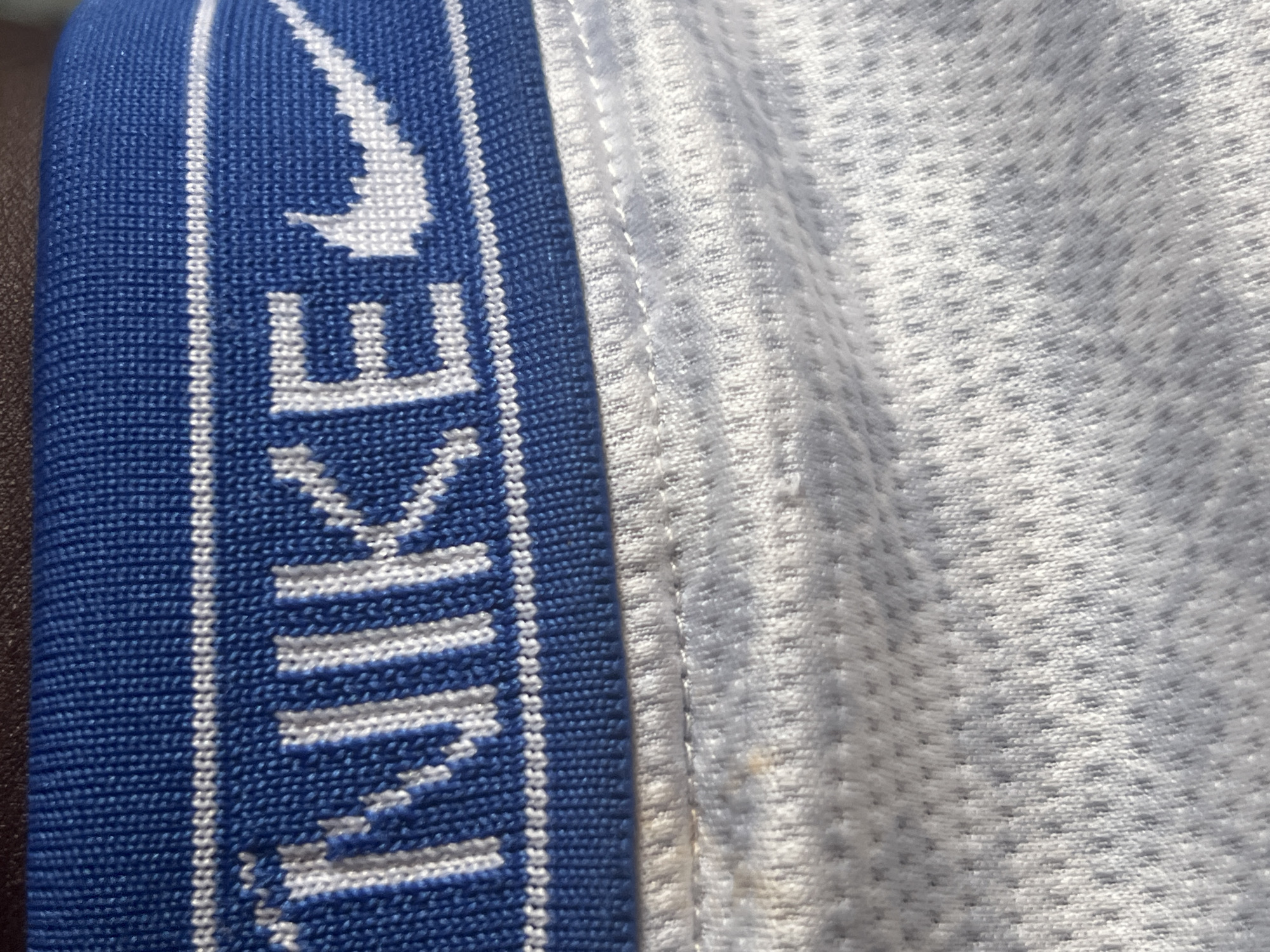 The image is a close-up of a blue Nike waistband on white fabric. The Nike logo and the word "NIKE" are visible in white lettering on the waistband. The white fabric below appears to be textured, possibly a mesh material. The scene is not located in Jauro Yinu, Nigeria.