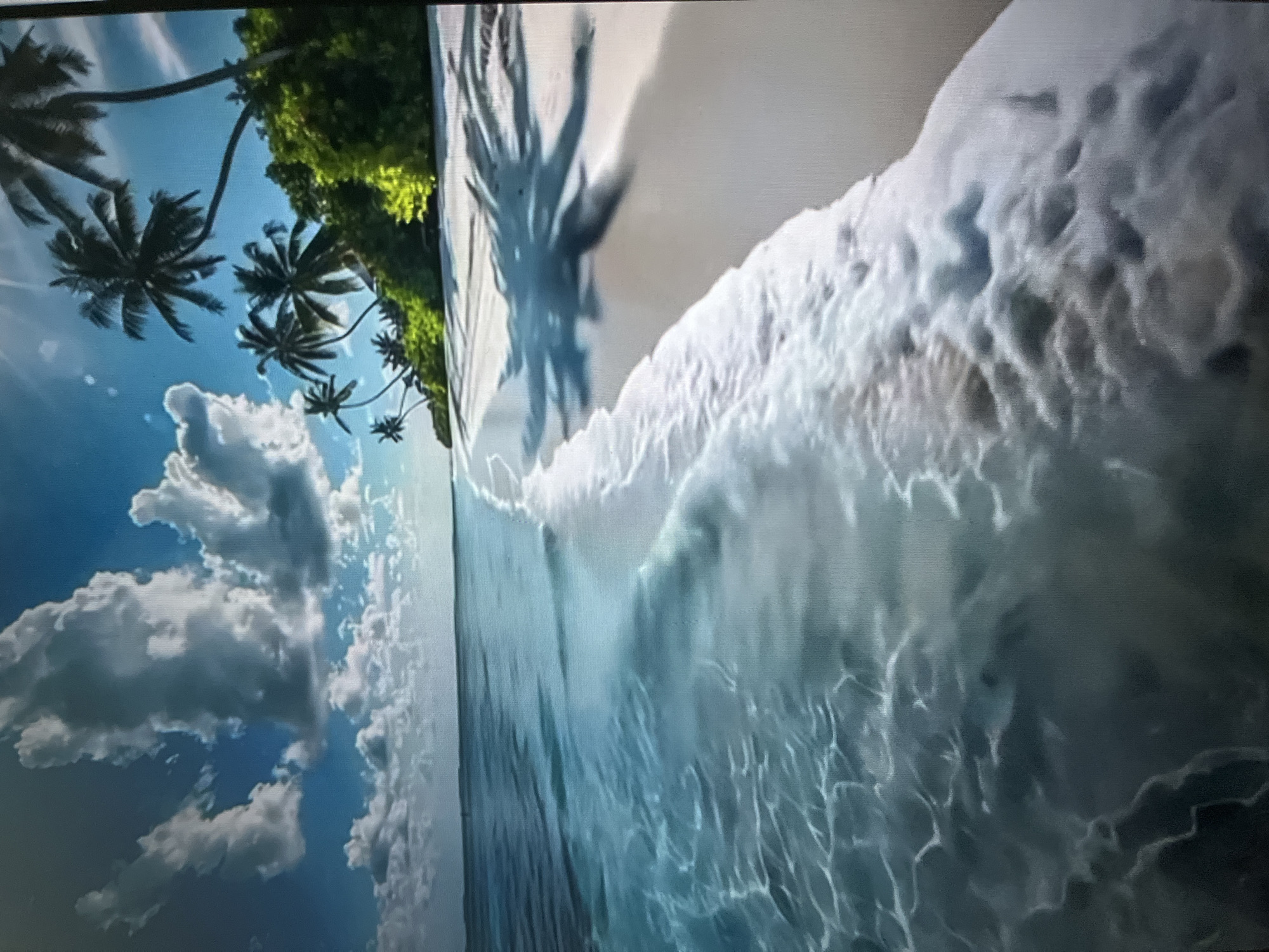 This is a serene tropical beach scene. Crystal clear turquoise water gently laps onto a pristine white sand beach. Palm trees with lush green foliage line the shore, casting dappled shadows on the sand. The sky is a vibrant blue, dotted with fluffy white clouds, and the sun shines brightly, creating a peaceful and inviting atmosphere. The image evokes a sense of tranquility and relaxation, characteristic of a tropical paradise.
