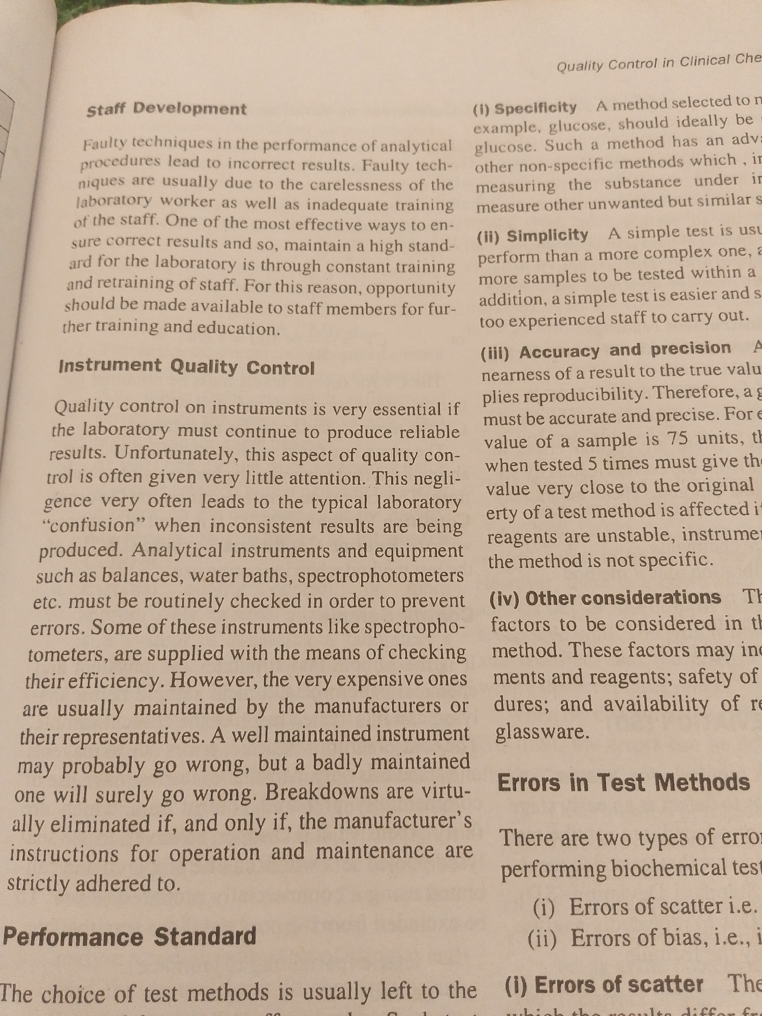 This media file is a close-up photograph of an open book, likely from a library or study setting. The book's pages are filled with text, suggesting an educational or informative context. The content appears to be academic, with headings like "Staff Development," "Instrument Quality Control," and "Performance Standard" visible on the left page, and "Quality Control in Clinical Che," "Errors in Test Methods," and other subheadings on the right page. The text discusses laboratory procedures, instrument maintenance, and types of errors in test methods. There are no people or clear indicators of a specific time of day or weather conditions. The setting is neutral, focusing solely on the content of the book. The text is in English. The location context of Jalingo, Nigeria, is not visually represented in the image itself but is provided as external information.