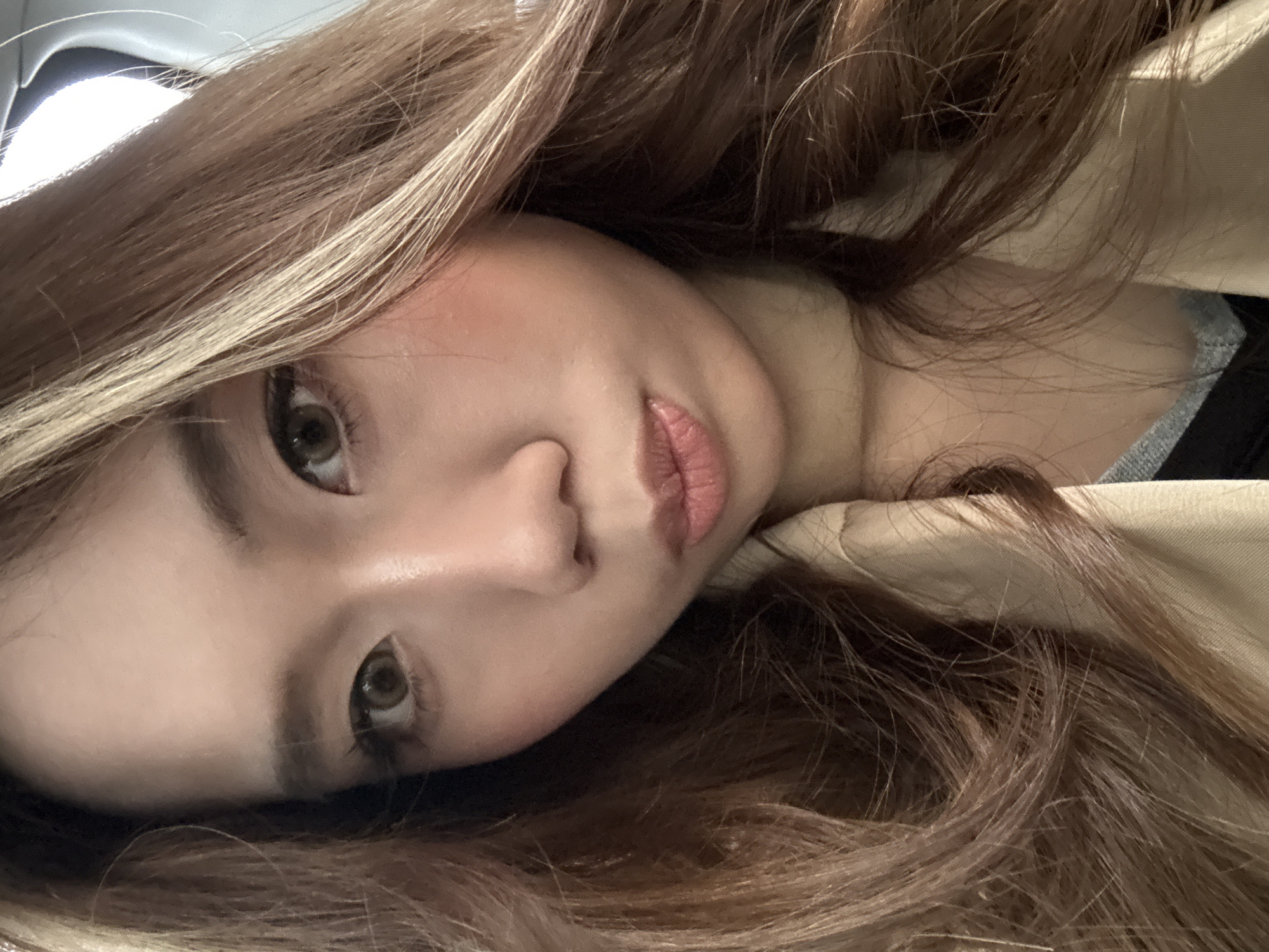 A close-up, slightly angled portrait of a woman with long brown hair with blonde highlights. She is wearing a light brown jacket with a visible collar. Her face is visible, showing her eyes, nose, and lips. The background is blurred, showing hints of light gray. There is no information that suggests this photo was taken in the city of Lanzhou, China.