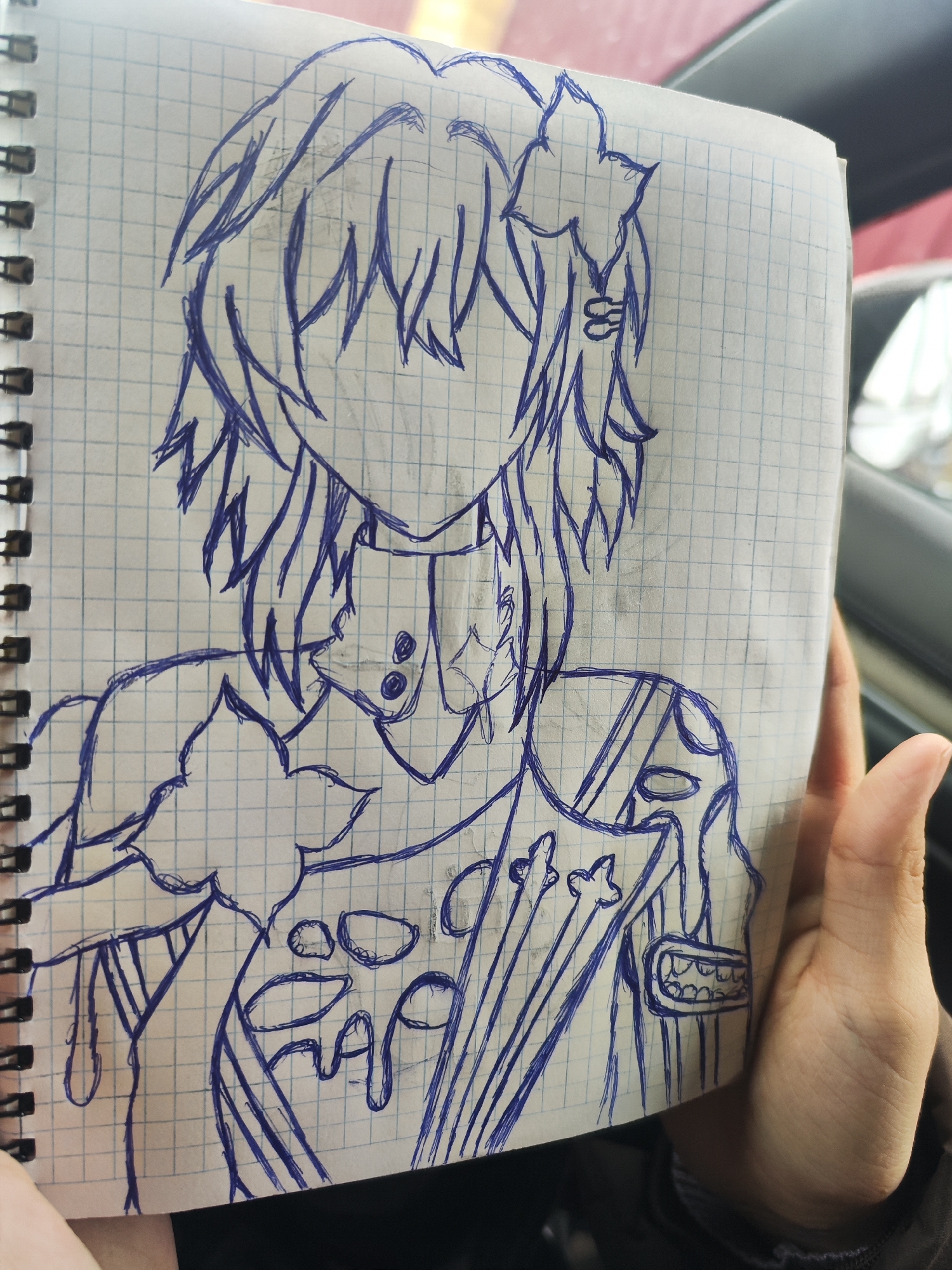 A person holds a notebook in their hands. The notebook contains a sketch of an anime-style character drawn in blue ink on graph paper. The character is from the shoulders up and appears to have short hair, decorative accents in their hair, and intricate clothing details. The character's face is not drawn in. The background shows an out-of-focus car interior, including a window and possibly a dashboard. No information suggests the picture was taken in Chaikovsky, Russia.