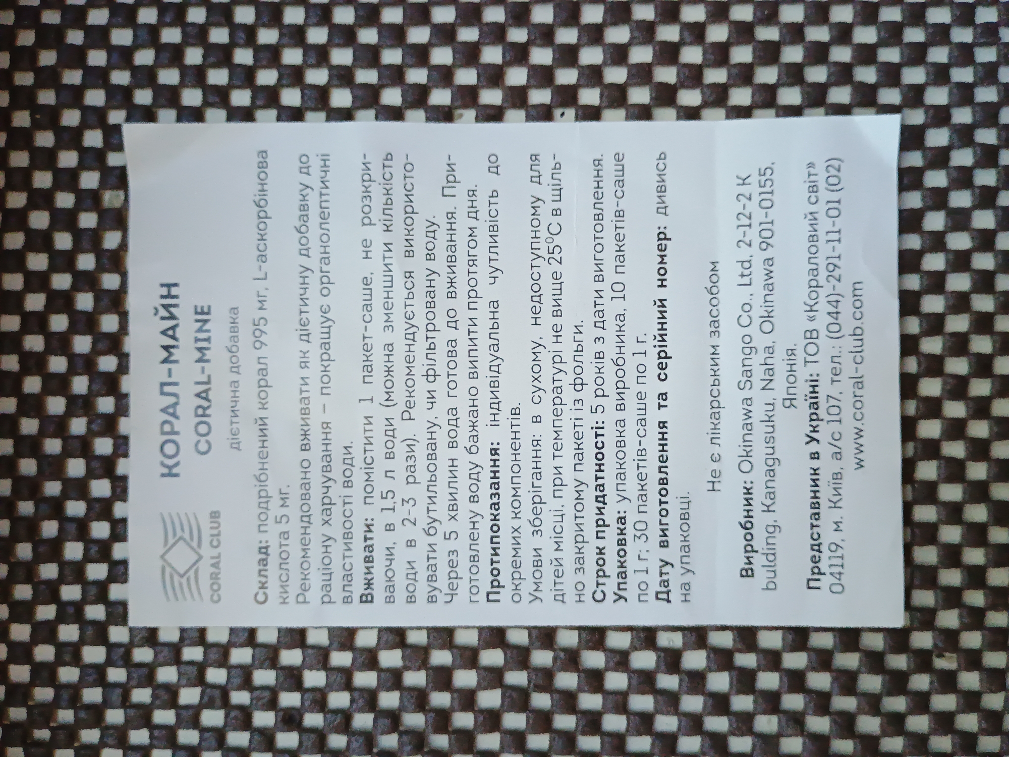The image shows a label with text in Ukrainian and English. The label is for "КОРАЛ-МАЙН" / "CORAL-MINE", which is described as a dietary supplement. The text provides information about the product's composition, usage instructions, contraindications, storage conditions, shelf life, packaging, and manufacturer. The manufacturer is listed as "Okinawa Sango Co., Ltd." in Japan, and the representative in Ukraine is "ТОВ «Кораловий світ»" located in Kyiv. There is no information in the image that would indicate the location of Zaporizhzhia, Ukraine. The image is a close-up, overhead shot of the label, which is printed on white paper and placed on a textured, dark background.