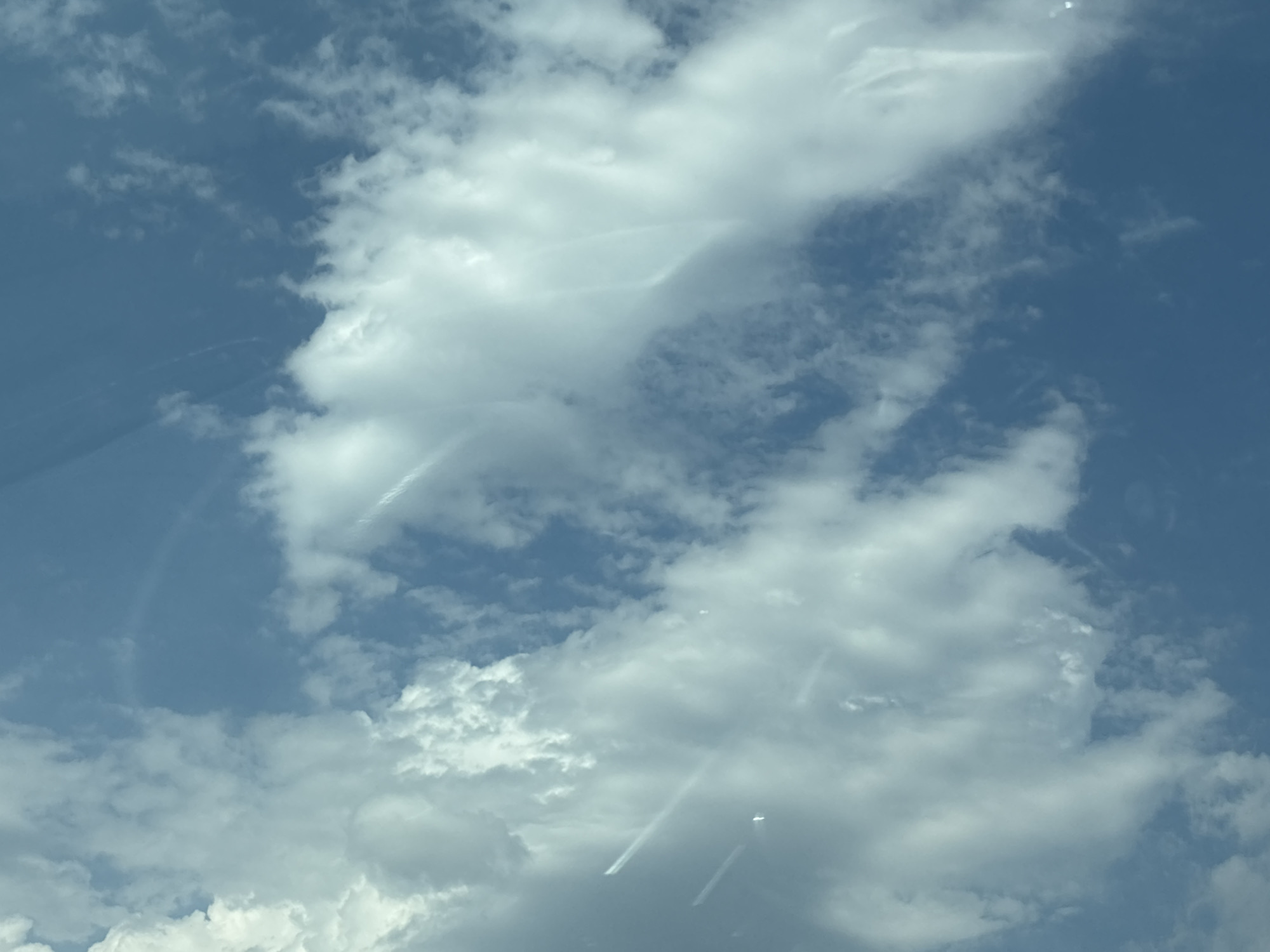 A cloudy sky is visible, with patches of blue peeking through. The clouds are a mix of white and grey, with some appearing fluffy and others more wispy. There are faint streaks or trails visible within the clouds, possibly from aircraft or atmospheric phenomena. The scene is an outdoor environment, with no specific structures or landmarks identifiable from the image alone to determine a precise location within Nagornoye, Russia. No people or actions are depicted.