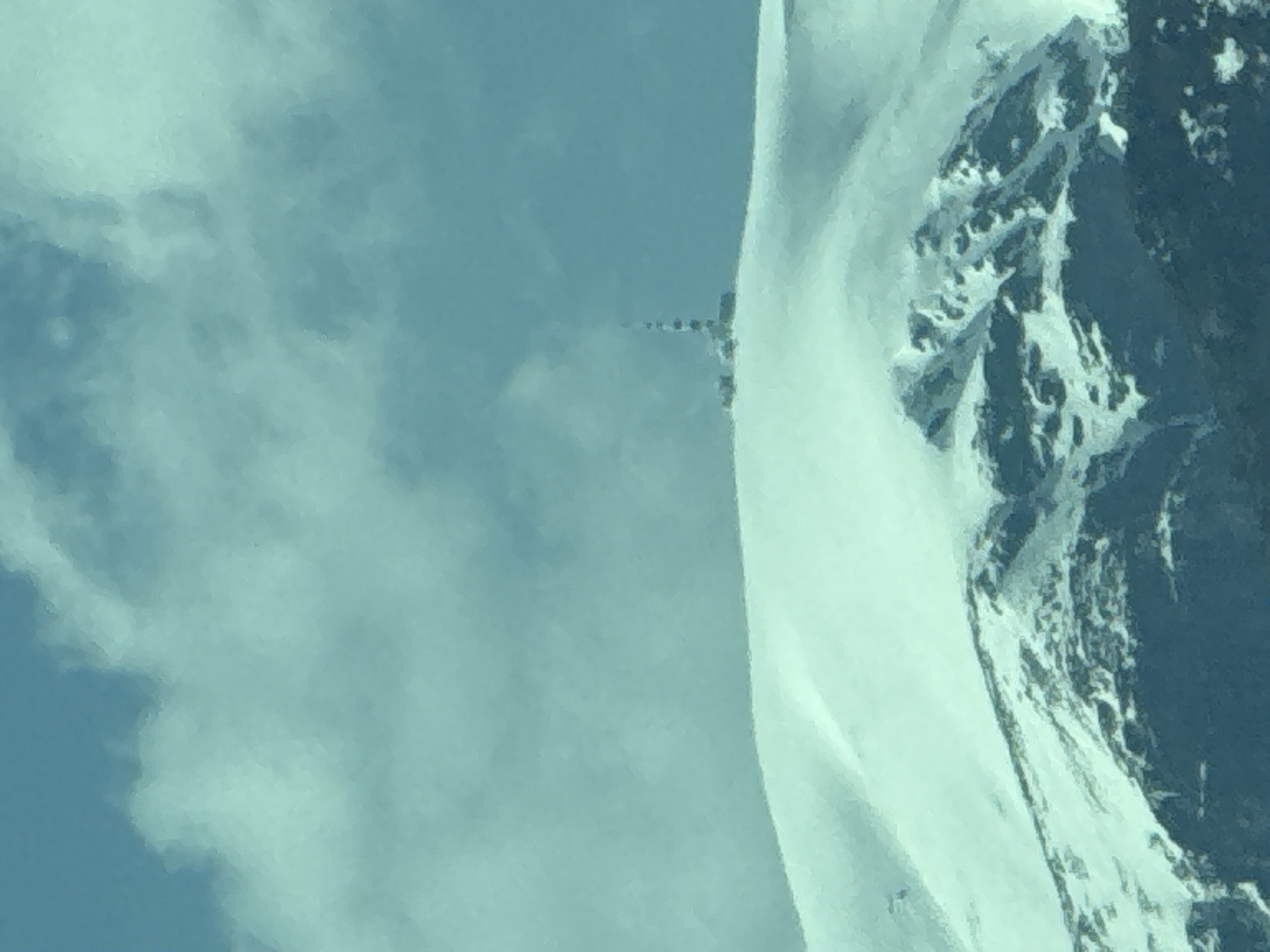 The image shows a snowy mountain ridge under a cloudy sky. A line of small objects, potentially a path or trail, can be seen leading up the ridge. The location of Manolovo, Bulgaria is not evident from the image.