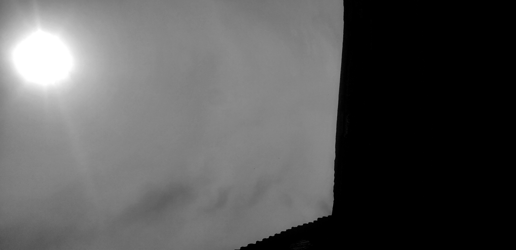 An overcast sky with the sun obscured by thick clouds dominates the image. The lower portion of the image shows an undefined, textured surface. The right side of the image is black, obscuring any details beyond this void. The image gives no indication of the location or any identifiable landmarks that would place it in Narayi, Nigeria. There are no people, actions, or interactions visible.