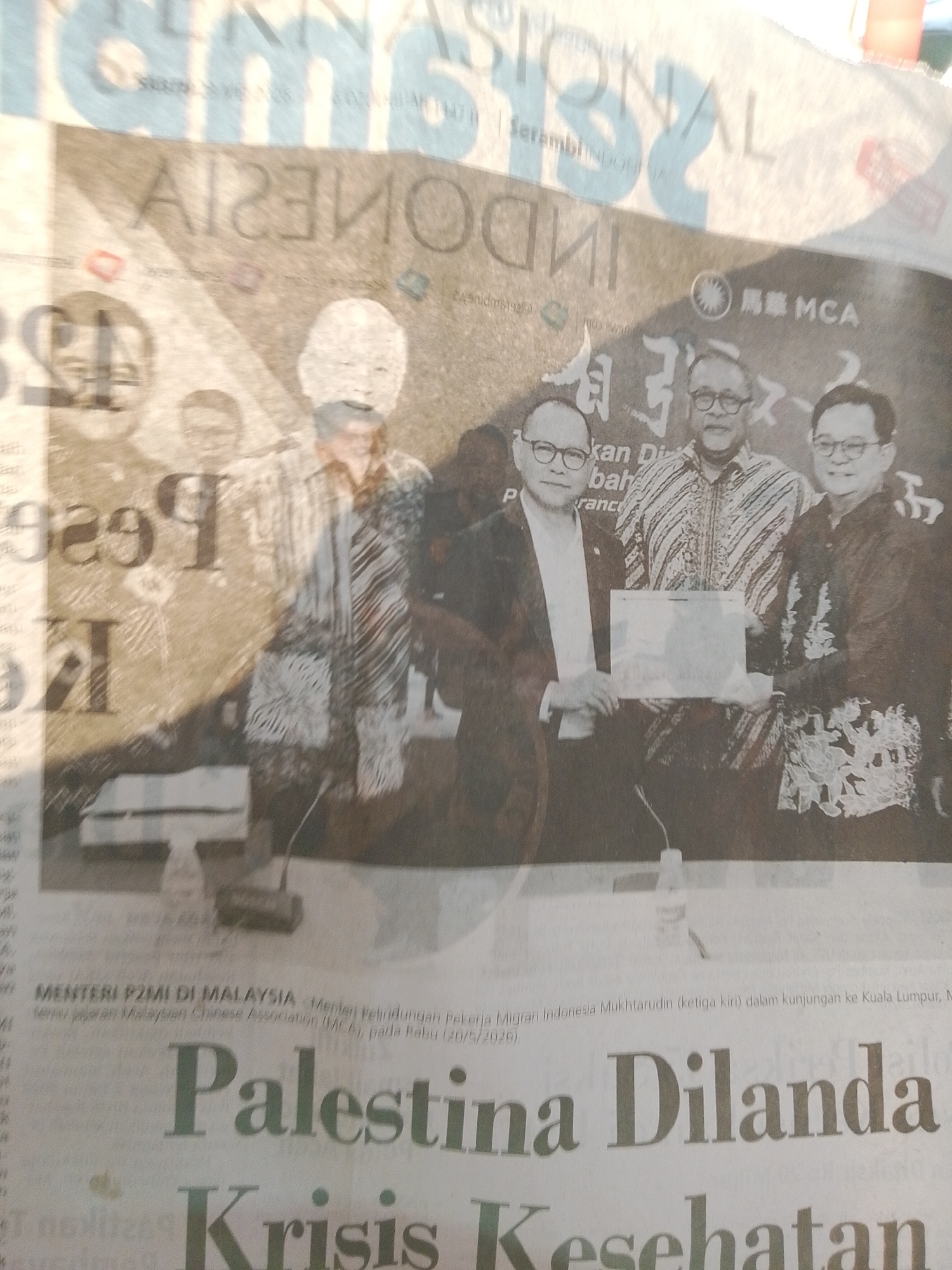 This is a black and white image of a newspaper article with an image of three men in suits standing together. The text in the article includes the words "INDONESIA", "MCA", "Palestina Dilanda Krisis Kesehatan", and "Menteri P2MI di Malaysia". The headline above the image appears to be about Palestinian health. The men in the photograph appear to be holding a certificate or plaque. The text indicates they are discussing Malaysian Chinese Association. The text also indicates that a man named Mukhtarudin is at the event. There is no indication that the image is in Lhokseumawe.