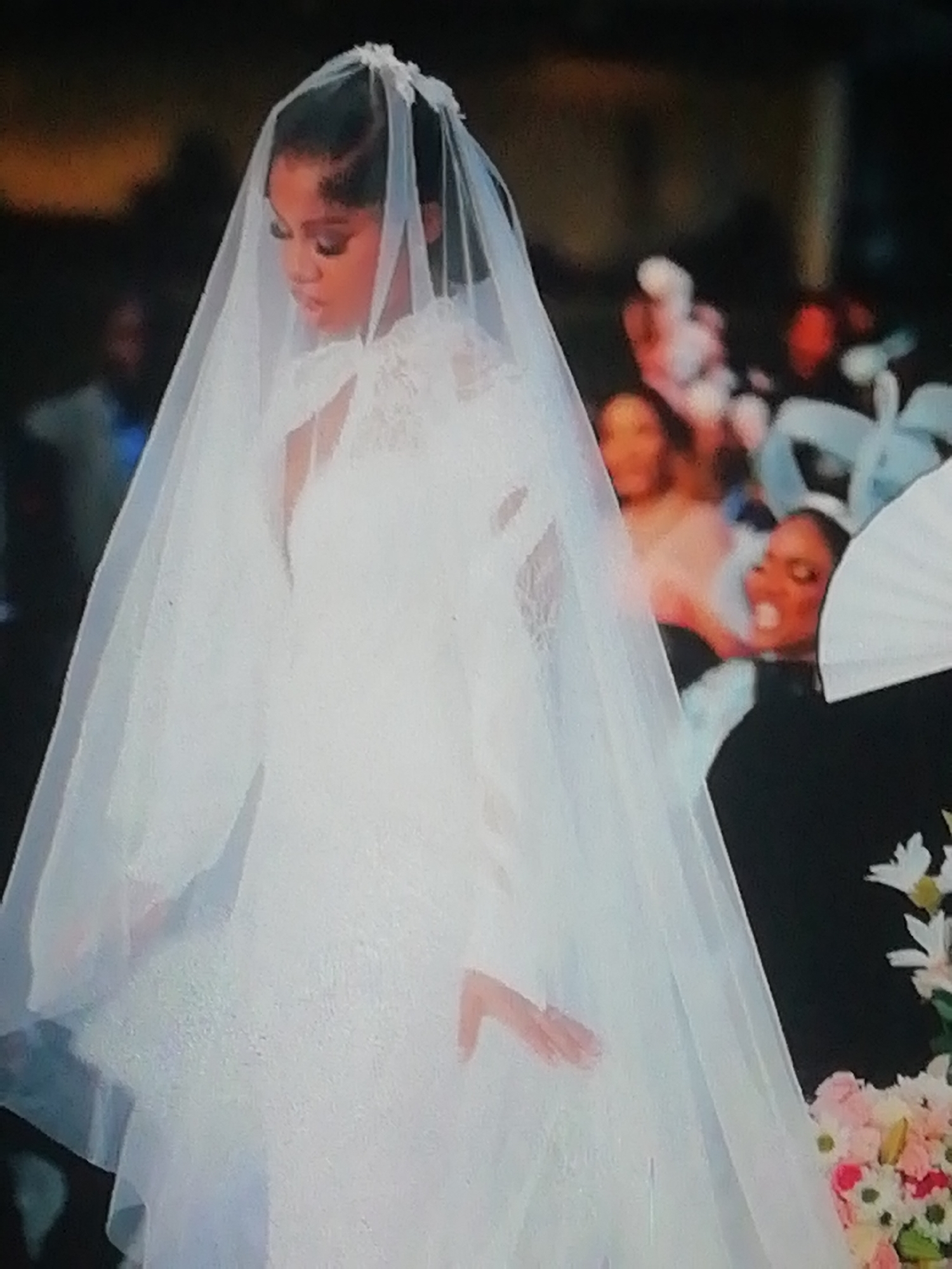 A bride stands in a white wedding dress and veil, attending a wedding ceremony. The background suggests a formal event with guests, floral arrangements, and formal attire. The location cannot be determined to be Enugu, Nigeria, solely based on the image.