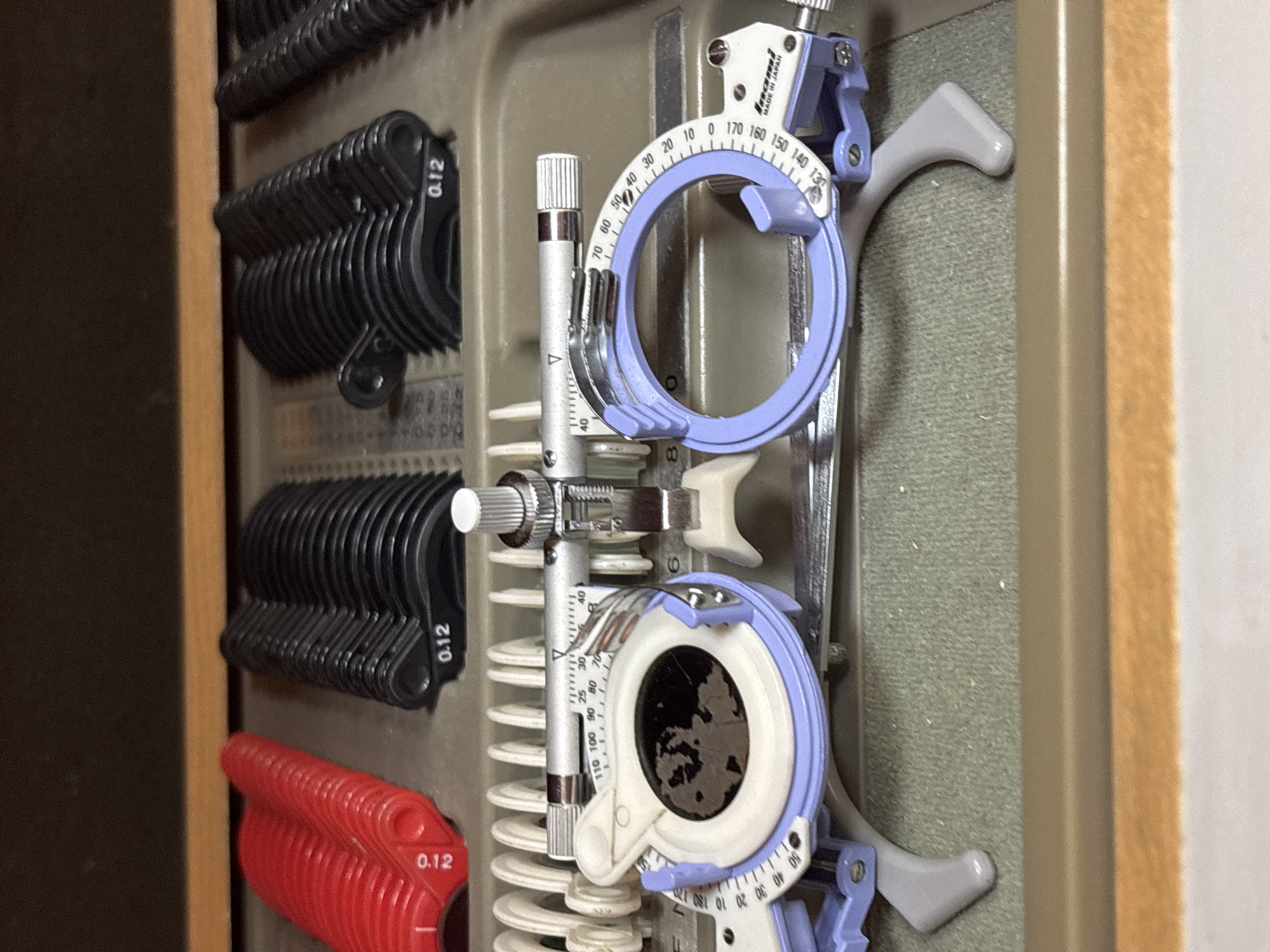 The image shows a trial frame and a trial lens set for optometry or ophthalmology use. The trial frame is made of metal and plastic, with an adjustable bridge and temples. It has slots for holding trial lenses of different powers. The trial lens set consists of multiple lenses in various diopters, stacked and arranged according to their power. The lenses are stored in a case or tray with marked values. The location, Plovdiv, Bulgaria is not evident in the image.