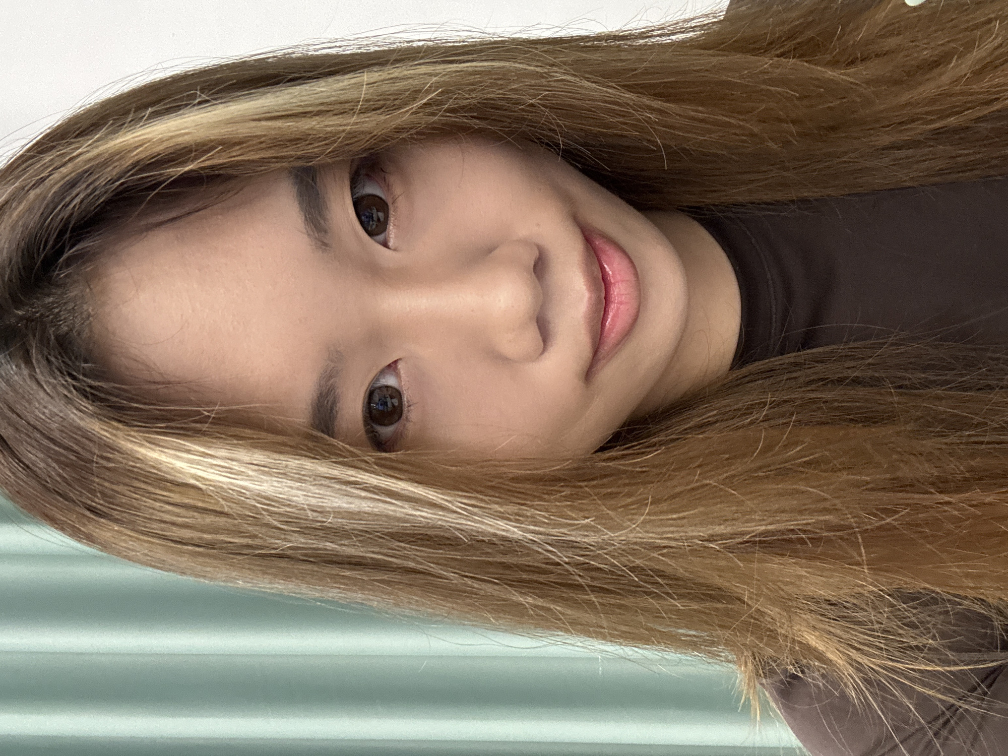 A person with light brown hair and brown eyes looks directly at the camera with a slight smile. The background is a light greenish-blue, and the person appears to be wearing a dark brown shirt. There is no information to confirm the location is in Nan'an District, China.