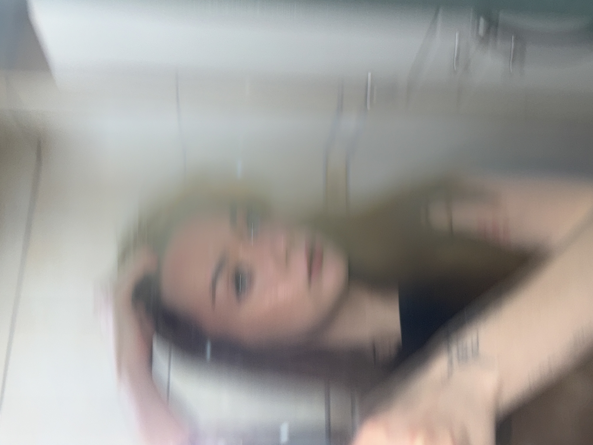 A blurry image of a woman with blonde hair and a tattoo on her arm, potentially in a bathroom setting. The background includes what appears to be a tiled wall with metal fixtures. There is no clear indication of the location being Kragujevac, Serbia.
