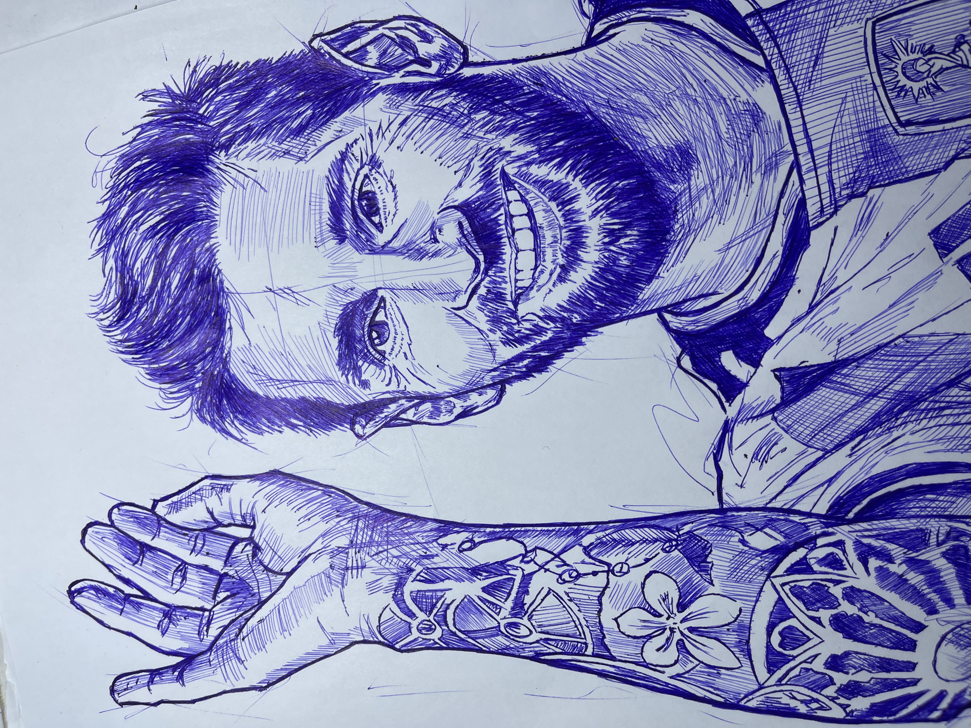 This is a close-up pen and ink drawing of Lionel Messi. The drawing is rendered in blue ink on a white background. Messi is depicted from the chest up, with his left arm raised and his hand open. He is smiling broadly, showing his teeth. His hair is tousled, and he has a full beard. His left arm is covered in a tattoo featuring a flower and geometric patterns. He is wearing a t-shirt with a crest on the left side of his chest. The drawing is characterized by a cross-hatching technique to create shading and form. There is no indication of the city of Jos, Nigeria, in this image.