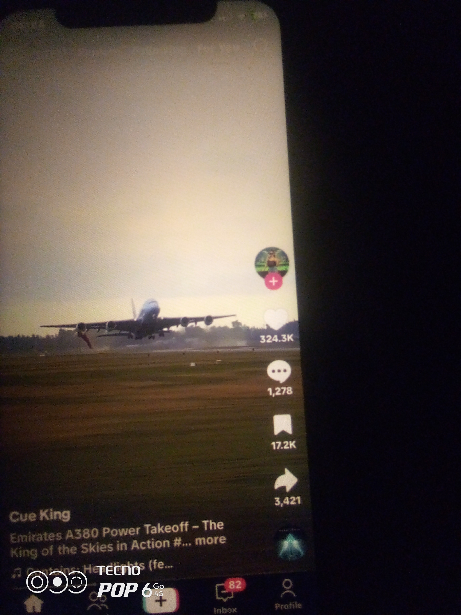 The image shows a TikTok video featuring an Emirates A380 aircraft during takeoff. The video is displayed on a smartphone, identified by the branding "POP 6 Go 4G". The background of the video is a runway with some foliage in the distance. On the right side of the video screen, there are interactive elements typical of social media platforms, including a profile picture with a plus sign, a heart icon with a count of 324.3K, a comment icon with a count of 1,278, and a share icon with a count of 3,421. The text overlay on the video reads "Cue King Emirates A380 Power Takeoff - The King of the Skies in Action #... more" and "Contains: H-lights (fe...". The smartphone is held in a dark environment, suggesting it's being used indoors or at night. There is no information within the image that indicates the location of Howayi, Nigeria.
