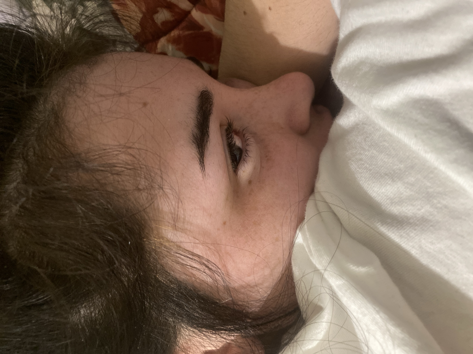 A person with brown hair and fair skin is lying on their side, partially obscured by a white cloth. The person's face is angled towards the camera. One eye is open and visible. Freckles are visible on the face. The background includes bedding with a pattern. There's no information present to suggest the location is Poltava, Ukraine.
