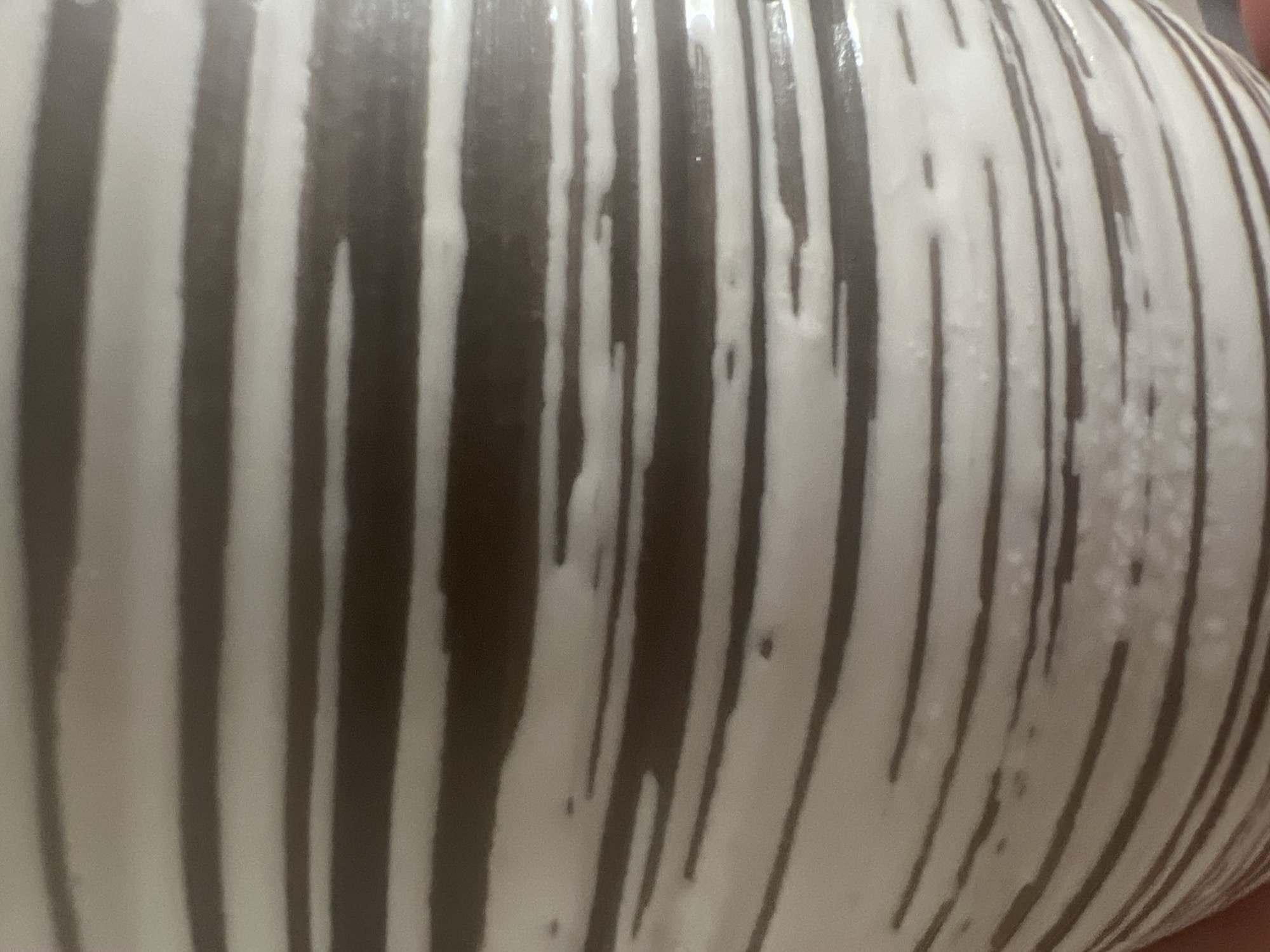 The image displays a close-up view of a ceramic object with a striped pattern. The stripes are horizontal and vary in thickness, alternating between a dark brown or grey color and a white or cream color. Some of the white stripes have an uneven, textured appearance with small darker specks or irregularities. The lighting suggests a smooth, possibly glossy surface. No other objects, people, or environmental details are visible in the image. The location in West Hartford, United States of America, is not discernible from the visual content of the photograph.