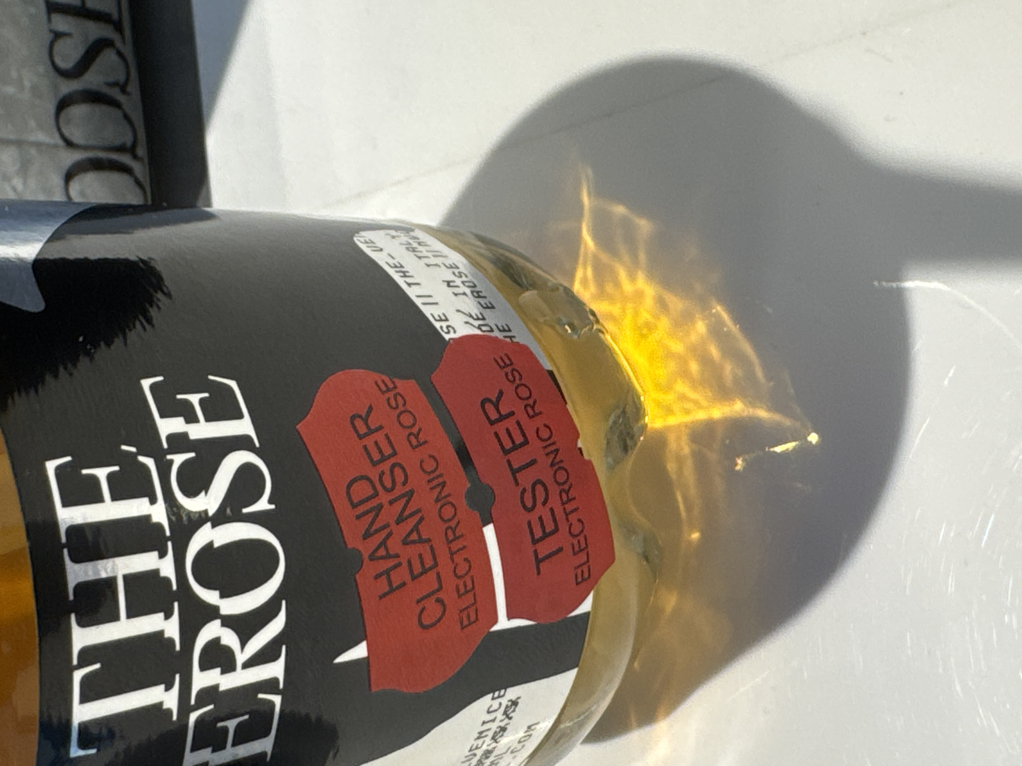 A bottle of "THE EROSE" brand hand cleanser is labeled as a "TESTER" and is "ELECTRONIC ROSE." The text also includes "HAND CLEANSER," "ELECTRONIC ROSE," and "SE IN ITALY." The bottle indicates Venice and an associated ".com" URL. The image also shows a shadow cast from the bottle onto a white surface. The city of Milan, Italy is not indicated.