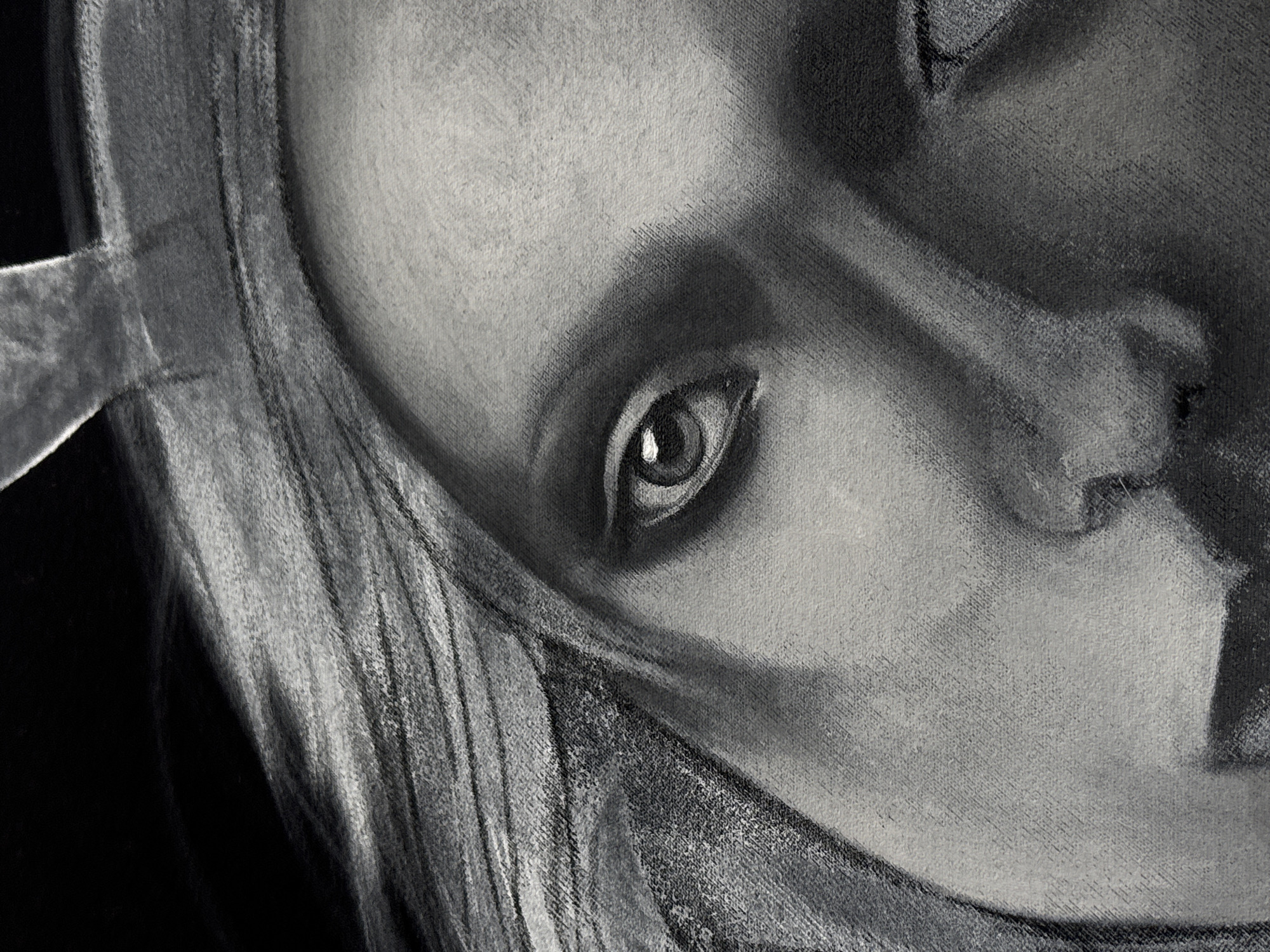 A close-up black and white charcoal drawing depicts a woman's face. The subject's right eye is prominently visible, with detailed rendering of the iris and pupil. Her nose and mouth are partially in shadow. A piece of metal lays across the top of her head and a lock of long hair lays alongside her face.
The location is not determinable from the image.