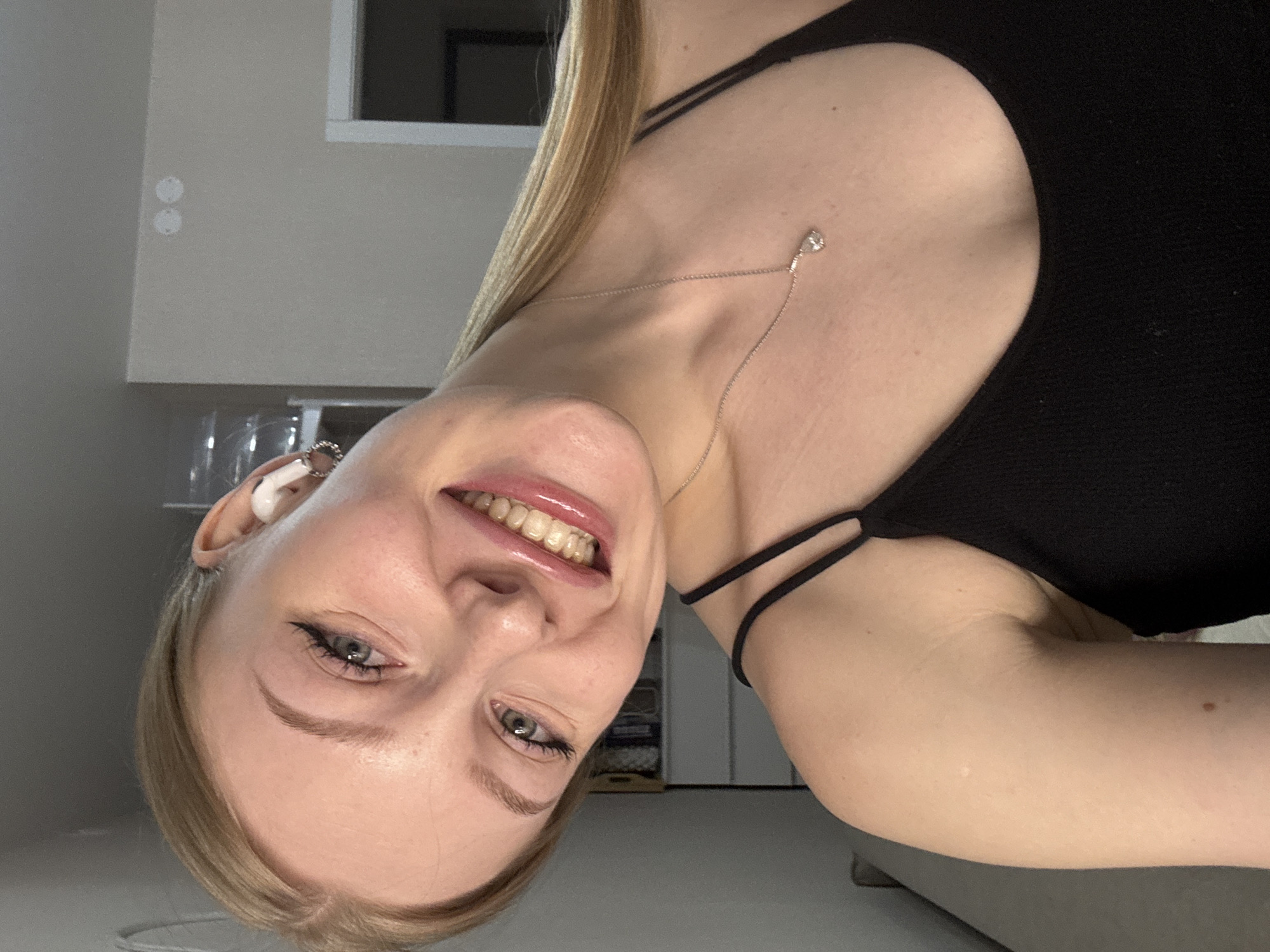 A woman with blond hair and blue eyes is smiling at the camera. She is wearing a black tank top and a silver necklace with a small pendant. She has eyeliner and lip gloss on. She appears to be indoors. There is no information provided indicating that the photo was taken in Perm, Russia.