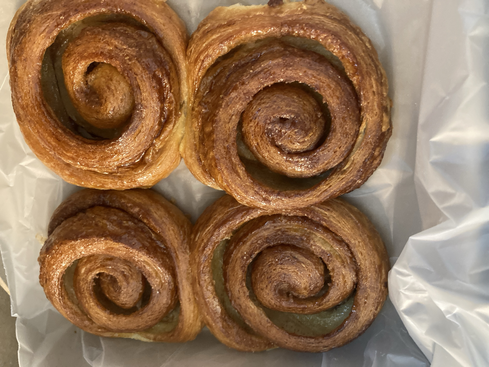 The image shows four pastries arranged in a square formation on a white surface, likely paper or parchment. The pastries are round and swirled, with a glossy, golden-brown exterior. The exact location is Unknown, Unknown.