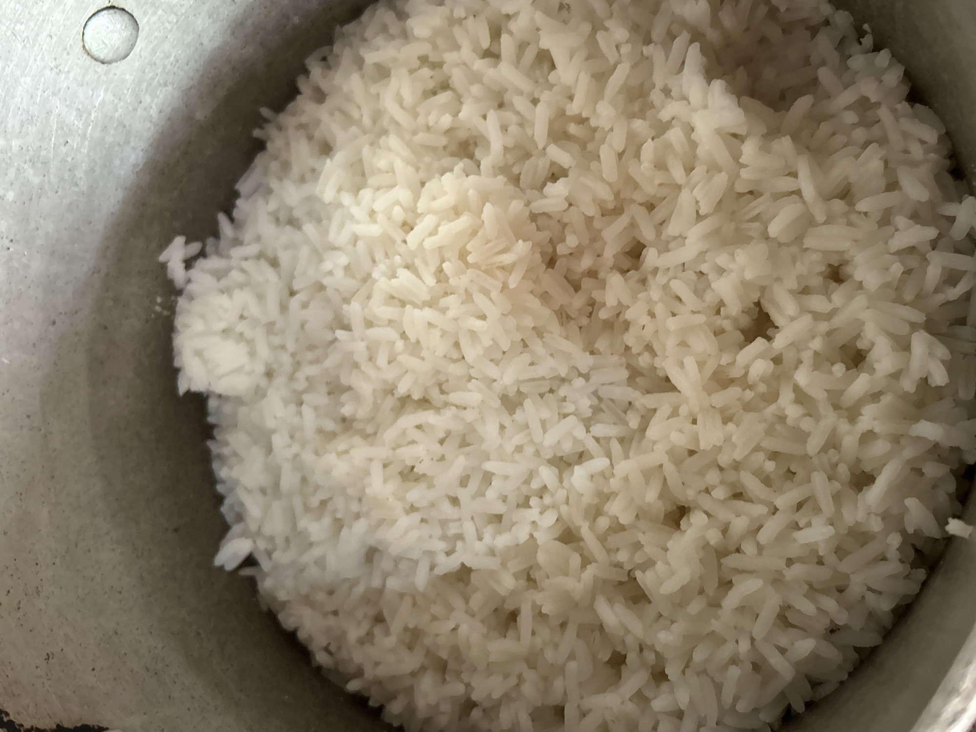 A close-up, overhead view shows a pot filled with cooked white rice. The rice is fluffy and appears to be long-grain. The interior of the pot is visible around the edges of the rice. There is a small, circular indentation on the upper right interior wall of the pot. The scene is indoors and the lighting is even. The location in Santa Ana, Venezuela is not discernable from the image.
