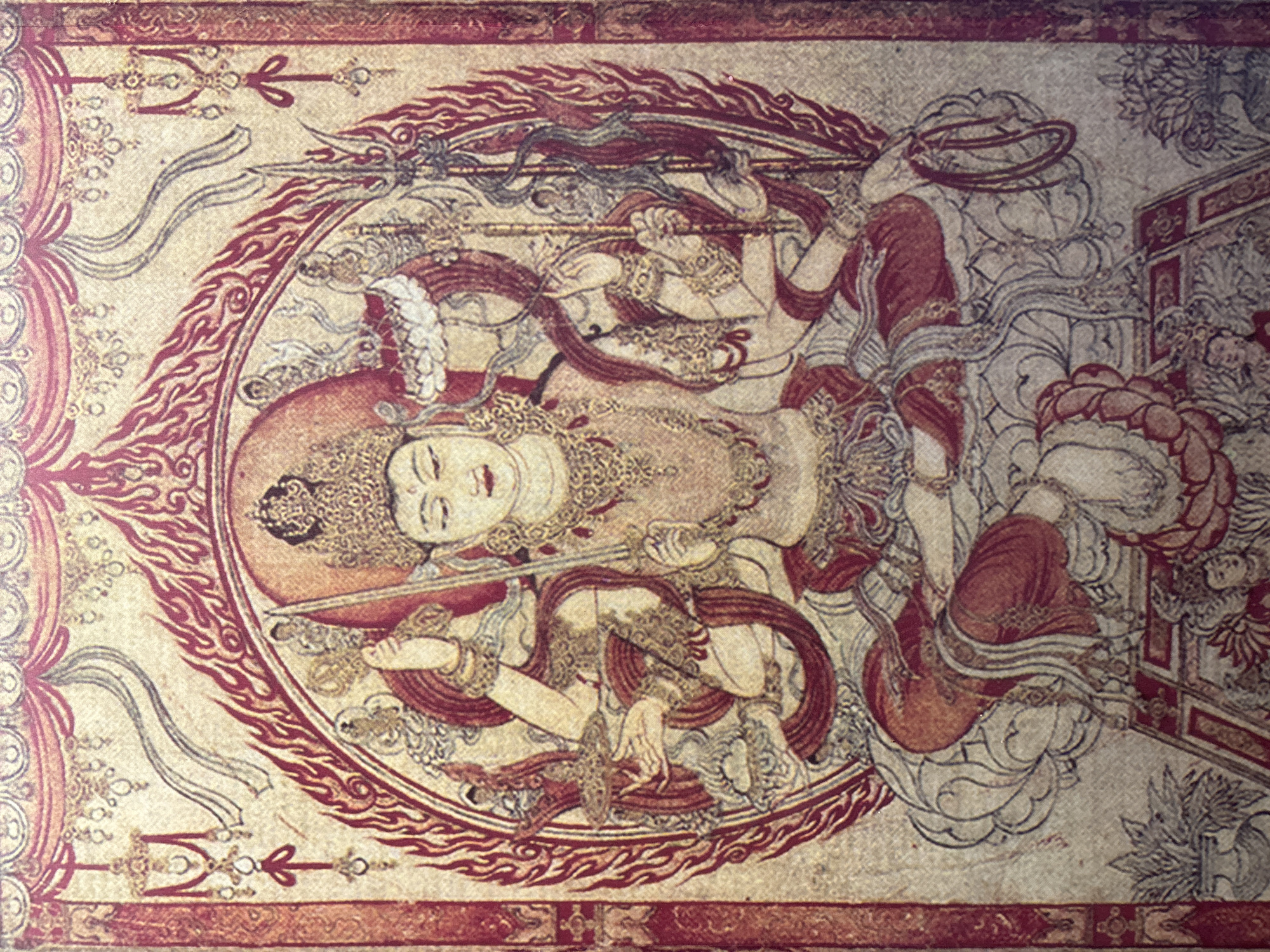 This image is a detailed photograph of a religious thangka painting, likely depicting a Buddhist deity. The painting features a central figure with multiple arms, adorned with an elaborate headdress and jewelry. The figure is seated in a lotus position on a stylized lotus flower, surrounded by a halo of flames. Multiple objects are held in the figure's hands, including swords and staffs. The background is a muted, textured canvas with decorative borders and intricate patterns. Small figures and decorative elements are also visible in the lower portion of the painting. The style suggests Tibetan or a related Himalayan Buddhist artistic tradition. The image does not depict any specific location within Dali City, China, as it is a standalone artwork and not a depiction of a geographical scene.