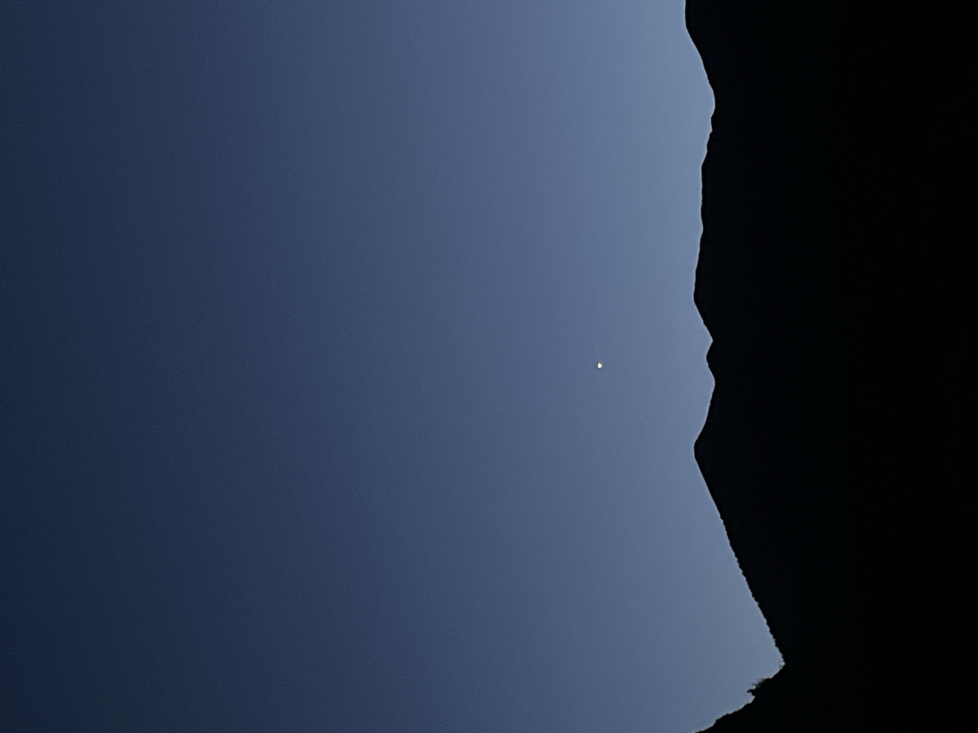 A solitary bright point, possibly Venus, shines in a deep blue twilight sky above the silhouetted jagged mountain range of Garmisch-Partenkirchen, Germany. The mountains are dark against the fading light.