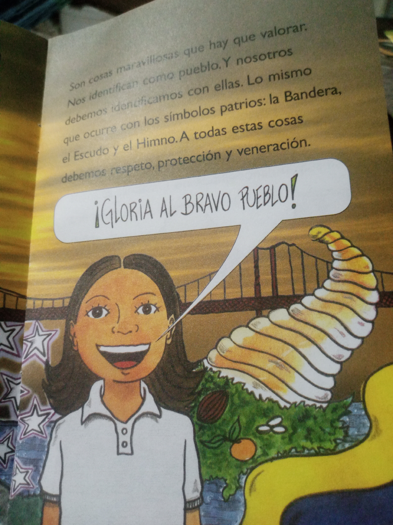 The image is a page from a children's book with an illustration and text. The text is in Spanish and reads: "Son cosas maravillosas que hay que valorar. Nos identifican como pueblo. Y nosotros debemos identificarnos con ellas. Lo mismo que ocurre con los símbolos patrios: la Bandera, el Escudo y el Himno. A todas estas cosas debemos respeto, protección y veneración. ¡GLORIA AL BRAVO PUEBLO!". The illustration depicts a young girl with dark hair, wearing a white polo shirt, smiling widely. She is positioned to the left of a golden, horn-shaped object that appears to be a "Cornucopia" or "Horn of Plenty," filled with greenery, an orange, and other small objects. Behind the girl and the cornucopia, a bridge with red railings and vertical supports is visible, against a sunset sky. The illustration style is cartoonish. The text and imagery are likely related to Venezuelan national symbols and patriotism, as indicated by the phrase "¡GLORIA AL BRAVO PUEBLO!" which is a line from the Venezuelan national anthem. However, there is no specific information within the image to pinpoint a location in the city of Santa Ana, Venezuela.