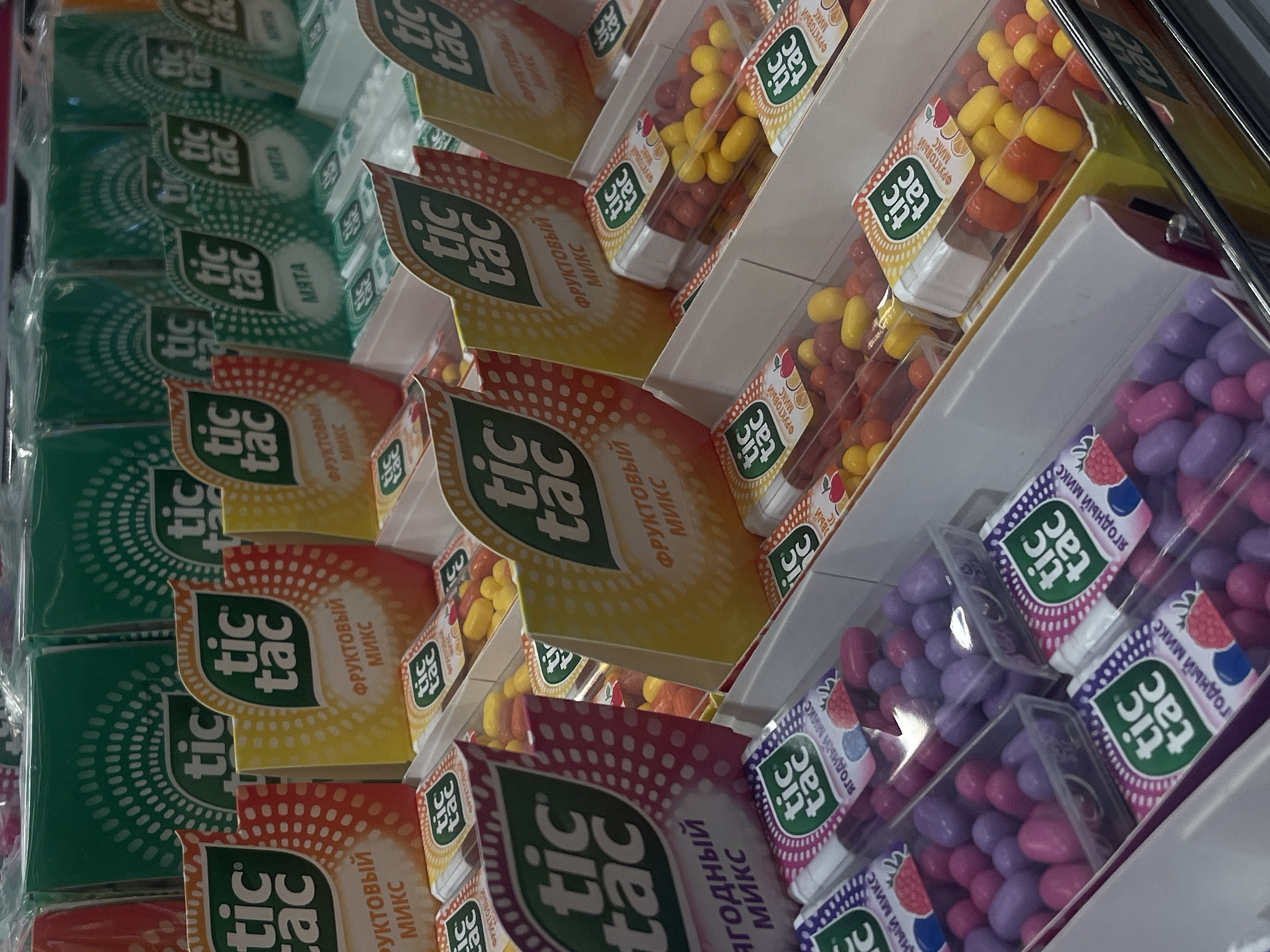 This image shows a shelf stocked with Tic Tac candies in a store. The flavors visible include "Mint," "Fruit Mix," and "Berry Mix." The candies are displayed in their plastic containers, arranged in rows. The image likely depicts a retail setting such as a store in Kommunarka, Russia.
