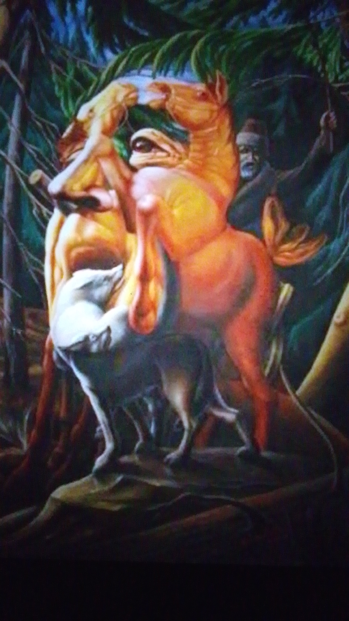 The image is a painting that uses an optical illusion to depict multiple figures. In the foreground, a white wolf appears to be interacting with a horse. The wolf's head forms part of the horse's body, while its hindquarters and tail are visible below. The horse itself is an orange and yellow color, and its body is cleverly integrated with the shapes of human faces.
One prominent human face is formed by the horse's hind legs and the wolf's body, with the wolf's head appearing as the nose and mouth of the face. Another human face is formed by the horse's head and mane, with its eye visible. The overall composition suggests a scene within a forest, with dark green foliage and tree trunks in the background. A figure of a man wearing a dark robe and a hat, with a beard, is visible in the upper right quadrant of the painting, holding what appears to be a weapon or a tool. His presence adds another layer to the complex imagery.
The image does not contain any information or visual cues that would allow for its location to be identified in the city of Aznakayevo, Russia.