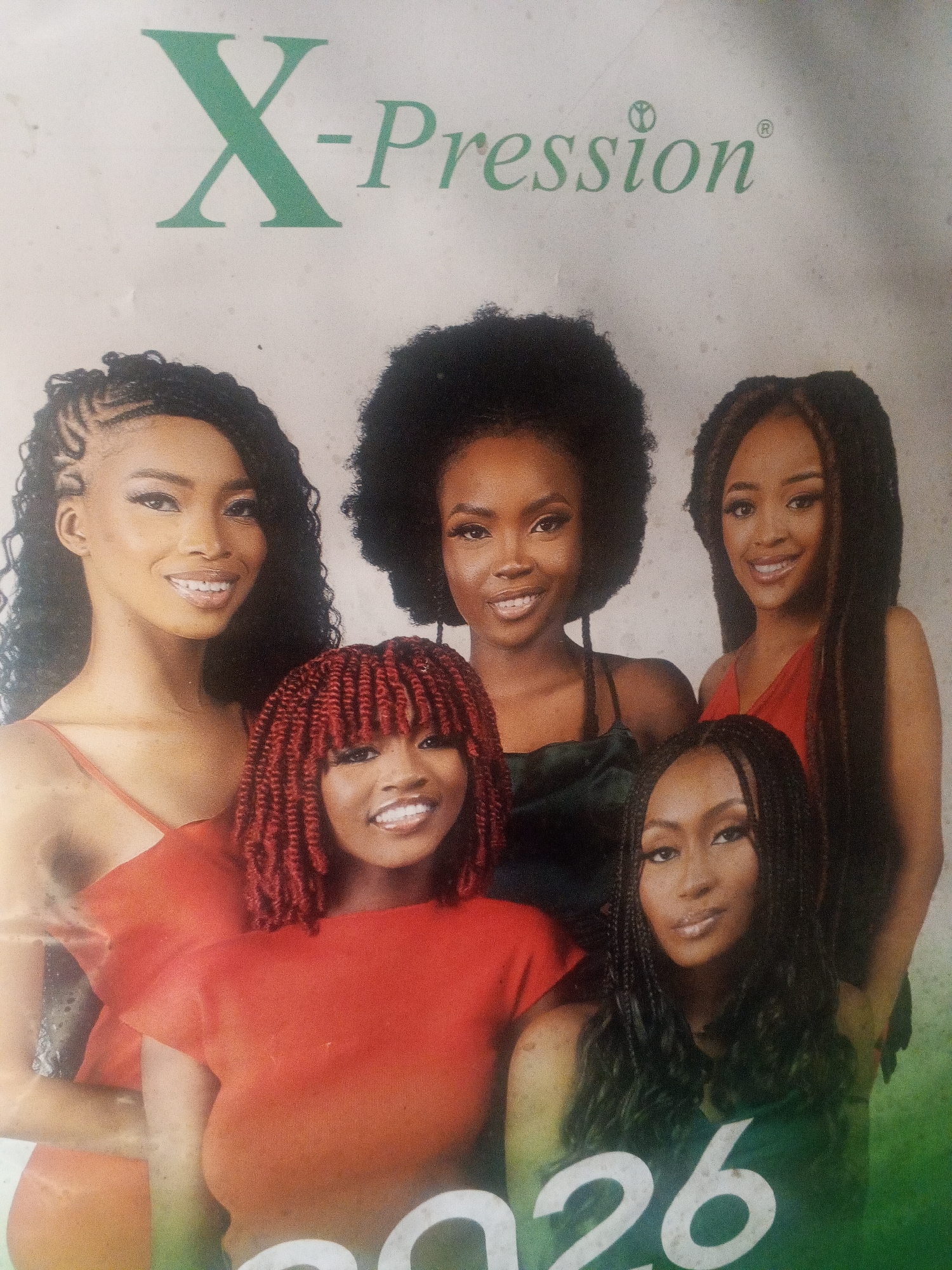 The image features a promotional poster for "X-Pression," a hair product brand, as indicated by the green logo at the top of the frame. Five Black women are centrally positioned.
From left to right, the first woman has braided hair with curls at the ends. The second woman has an afro hairstyle. The third woman has long, straight hair with light brown highlights. The fourth woman, positioned in front, has short, red twisted braids. The fifth woman has long, braided hair.
The women are dressed in various solid color tops, including red, green, and black. The number "26" is partially visible at the bottom of the image, with a color gradient from green to white.
The location of the poster is unknown.