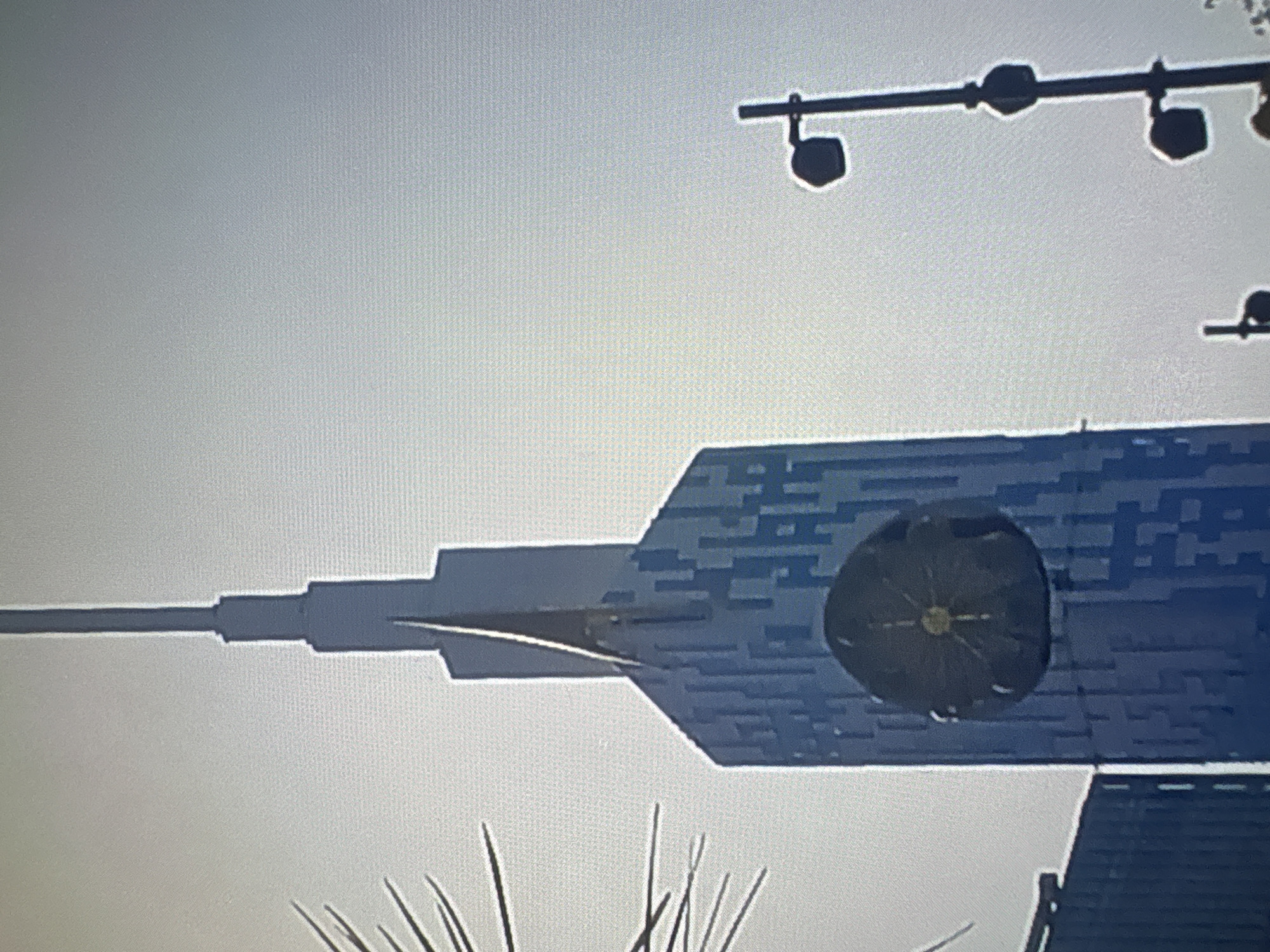 This image captures a view of the Batumi Technological University building in Batumi, Georgia. The building is tall and modern, with a distinctive blue facade composed of rectangular panels. A prominent circular clock face is affixed to the building's exterior. To the right, a street lamp with multiple lights is visible against a hazy sky. The background is a light, overcast sky, characteristic of an urban environment. The overall impression is one of modern architecture within a city setting.