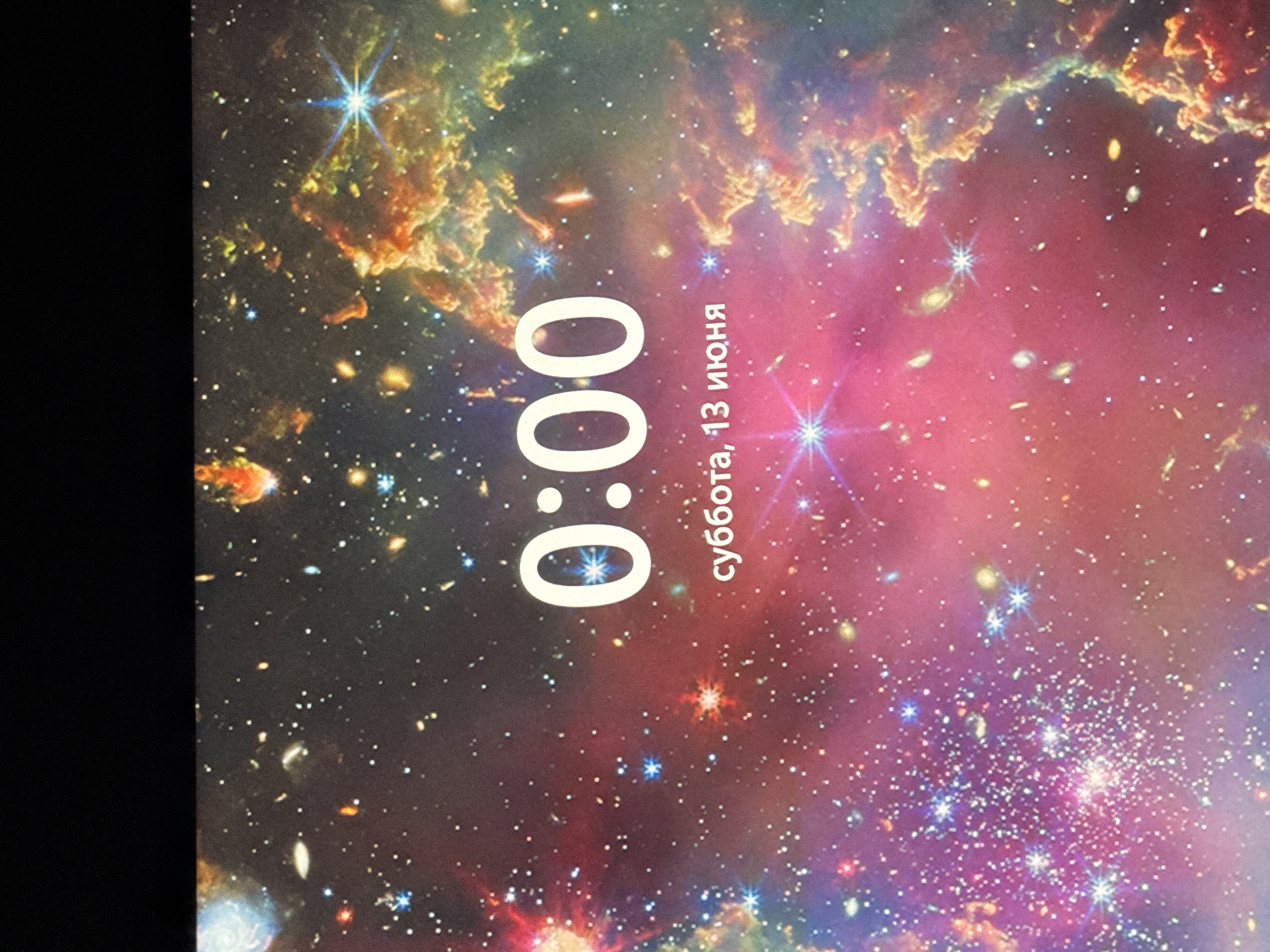The image shows a digital display with a time of 0:00 and the date "суббота, 13 июня" which translates to "Saturday, June 13th." The background is a vibrant, colorful image of a nebula and stars, characteristic of a space or galaxy theme. There is no indication of the city of Bellheim, Germany within the image itself. The display is a static image, likely from a phone or computer screen, with no people or ongoing actions depicted.