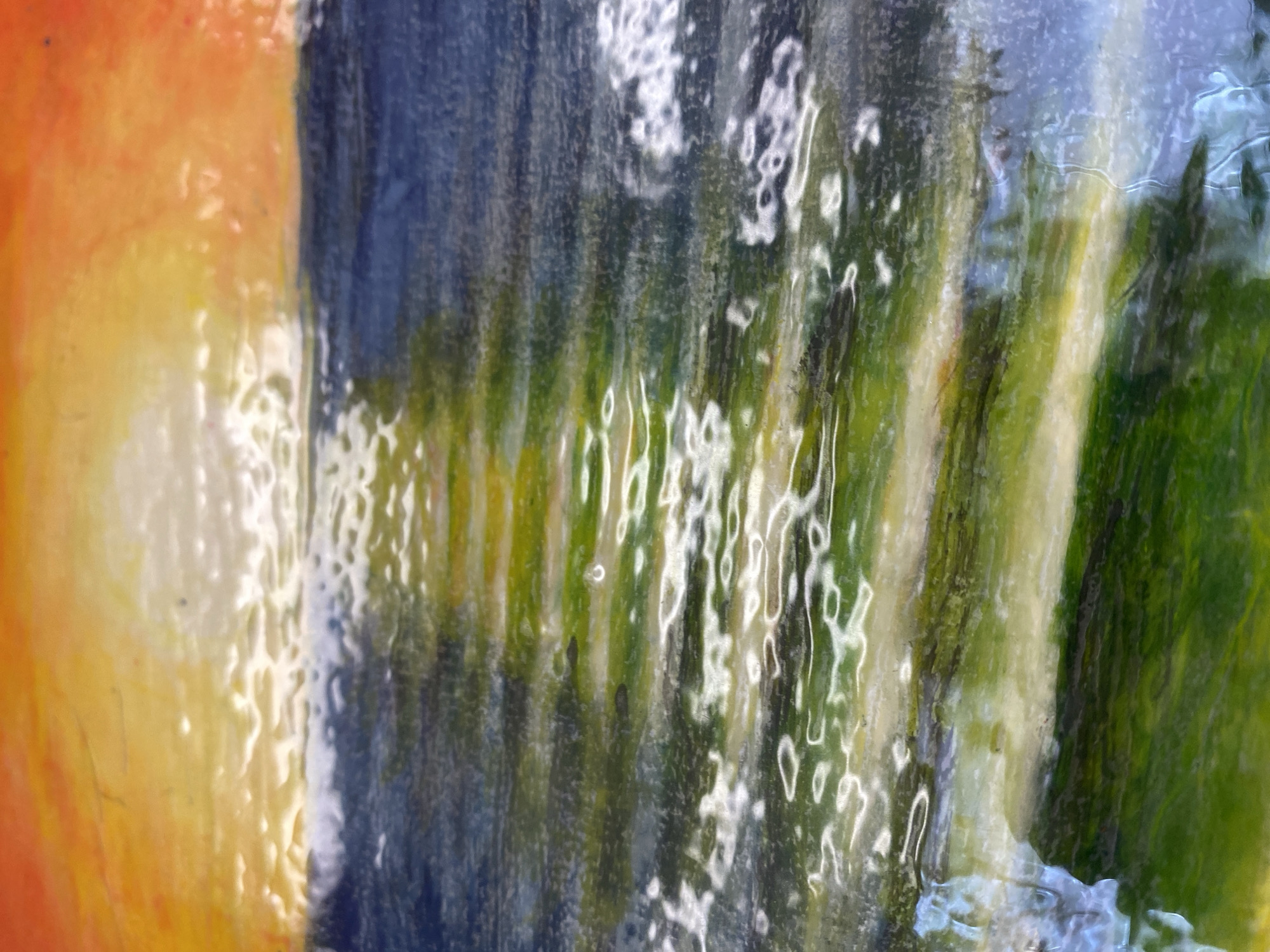 The image is a close-up, abstract-looking shot with a vibrant mix of colors: orange, yellow, blue, green, and white. The texture appears glossy and slightly distorted, as if viewed through a wet surface or rippled glass. The colors are arranged in vertical bands or streaks, with the orange and yellow on the left transitioning to darker shades of blue and green on the right. There are white, almost bubble-like or water-like patterns superimposed on the color transitions, adding to the impression of wetness or reflection. Given the description requirements, the image does not inherently reveal a precise location in the city of Chaikovsky, Russia, specific people, actions, or objects other than the color and textural elements described. Therefore, only the visual details can be factually presented.