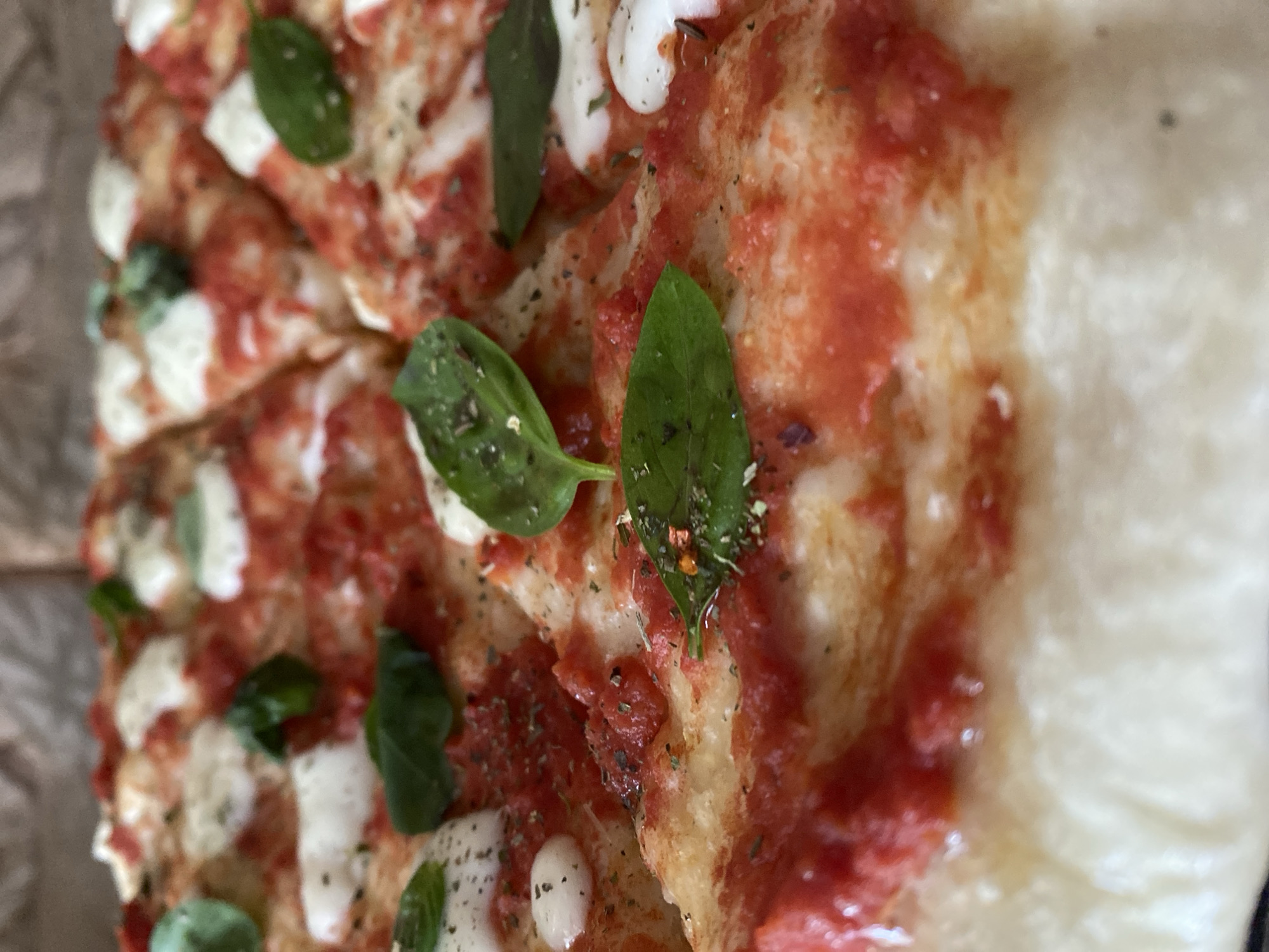 A close-up shot features a whole margherita pizza that has been cut into slices. The pizza has a thick crust and is topped with tomato sauce, fresh mozzarella, and basil leaves. The toppings are spread evenly across the pizza, and the cheese is melted and bubbly. The basil leaves are a vibrant green and are scattered across the pizza, adding a fresh aroma to the dish. The pizza is arranged on a flat surface, and the background is blurred, drawing attention to the delicious-looking pizza.