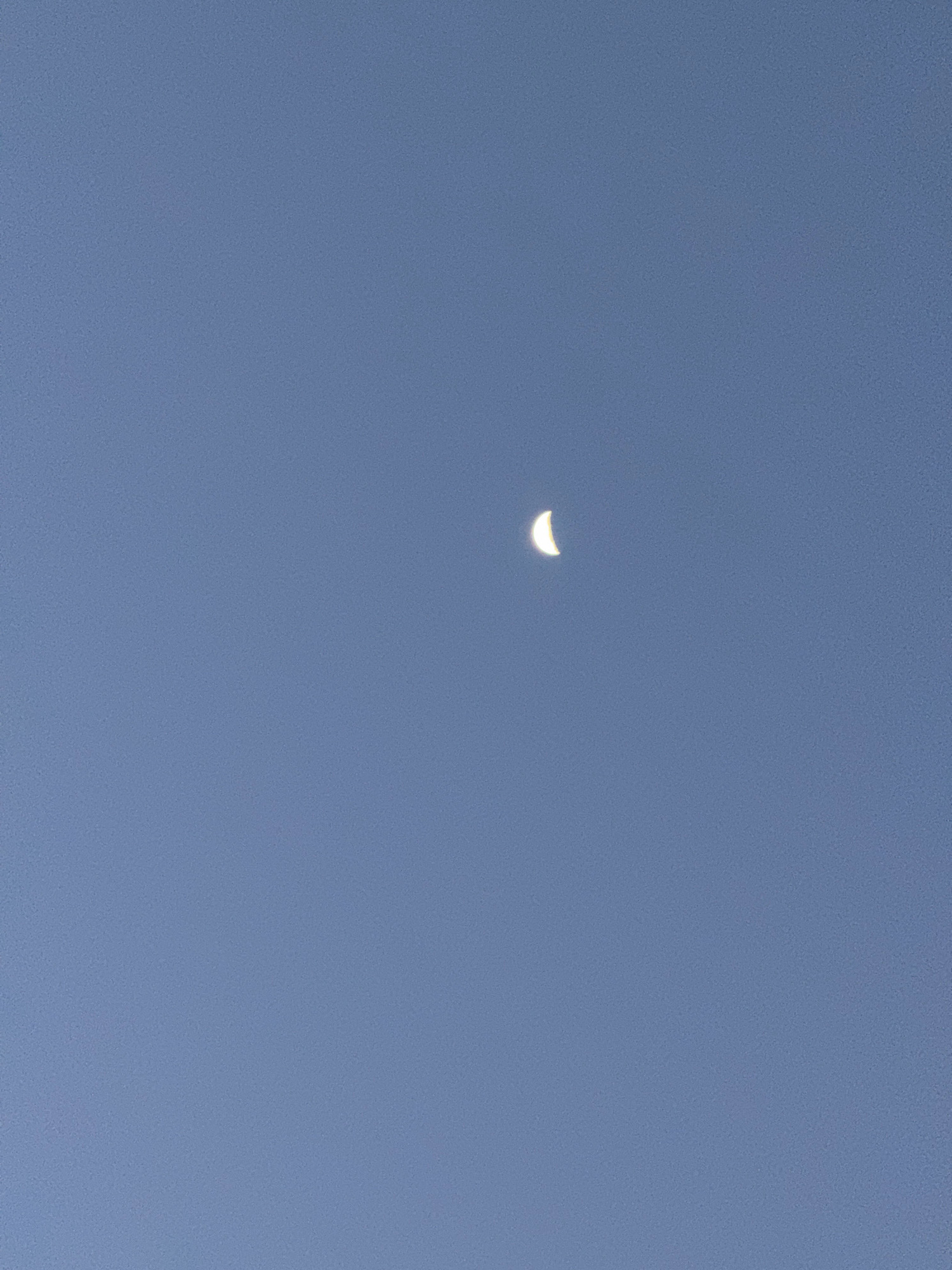 The image shows a crescent moon in a clear, blue sky. There are no buildings or people visible.
