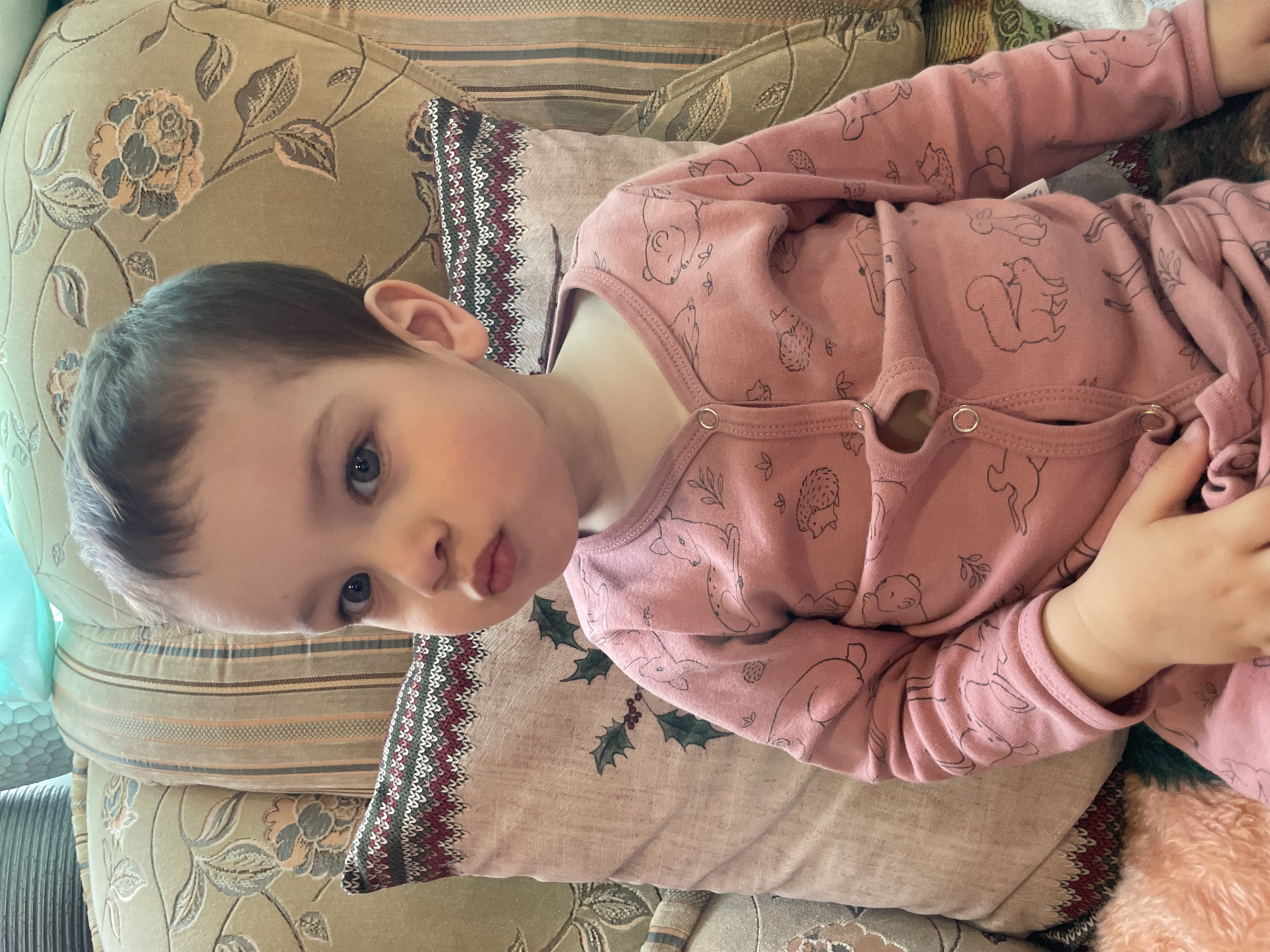 A child is lying on a patterned sofa or cushion. The child is wearing pink patterned pajamas. The exact location in the city of Zav'yalovo, Russia cannot be determined from the image.