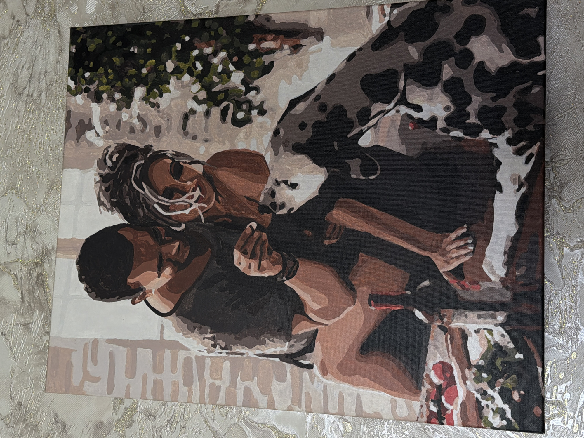 A painting depicts a couple and a dog in an outdoor setting. The couple, with darker skin tones, is seated. The man, on the left, has short dark hair and is wearing a dark t-shirt. The woman, on the right, has dark hair styled up and adorned with white streaks. She is wearing a strapless top. The man is holding a small white object, possibly food, near the dog's mouth. The dog is a Dalmatian with black spots on a white coat, and it is leaning in to take the object. In the foreground, to the left, there is a table with a plate of red fruits, possibly strawberries, and a bottle of red wine. The background shows a textured wall and some greenery. The overall lighting suggests a sunny day.