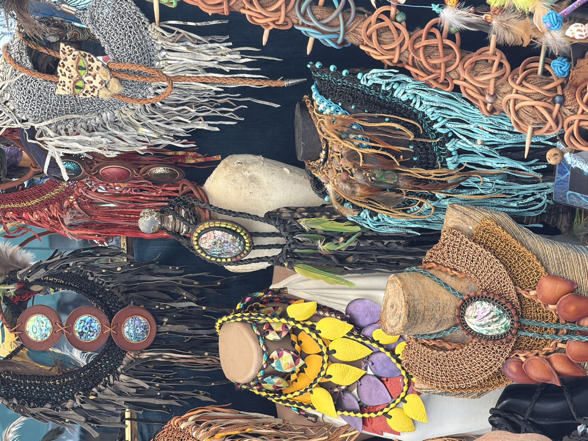 A collection of artisan jewelry is displayed. Various headbands and necklaces, featuring leather, feathers, beads, and stones, are arranged on mannequins. The scene, identified as being located in Tel-Aviv, Israel, presents a vibrant array of handcrafted accessories.