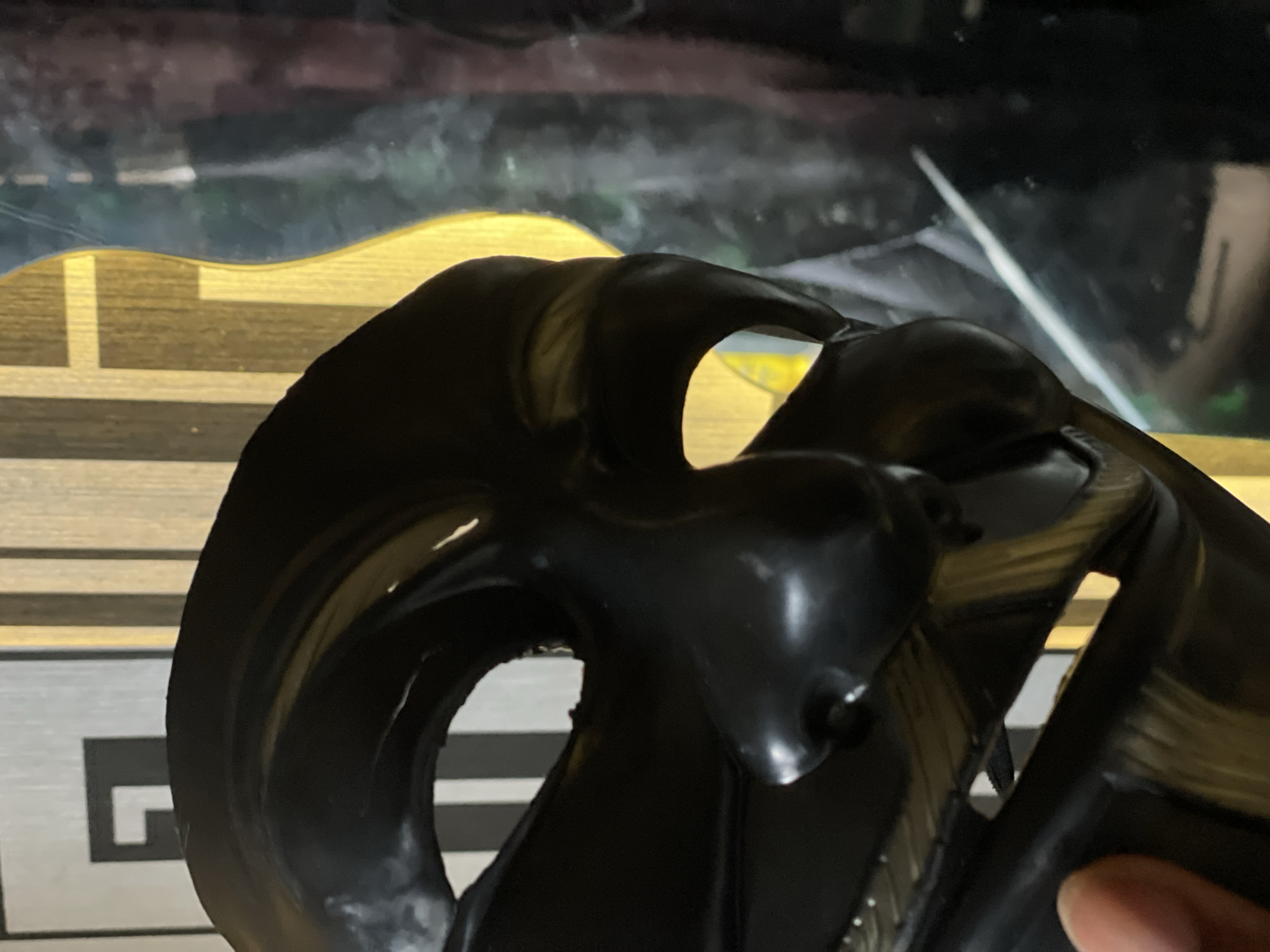 The image shows a close-up of a black, abstract object with irregular shapes and openings. It is positioned in front of a background that includes a striped pattern and a blurred, dark area. There are no discernible people, actions, or interactions. The environment and location in Lokoja, Nigeria are not evident from the details in the image.