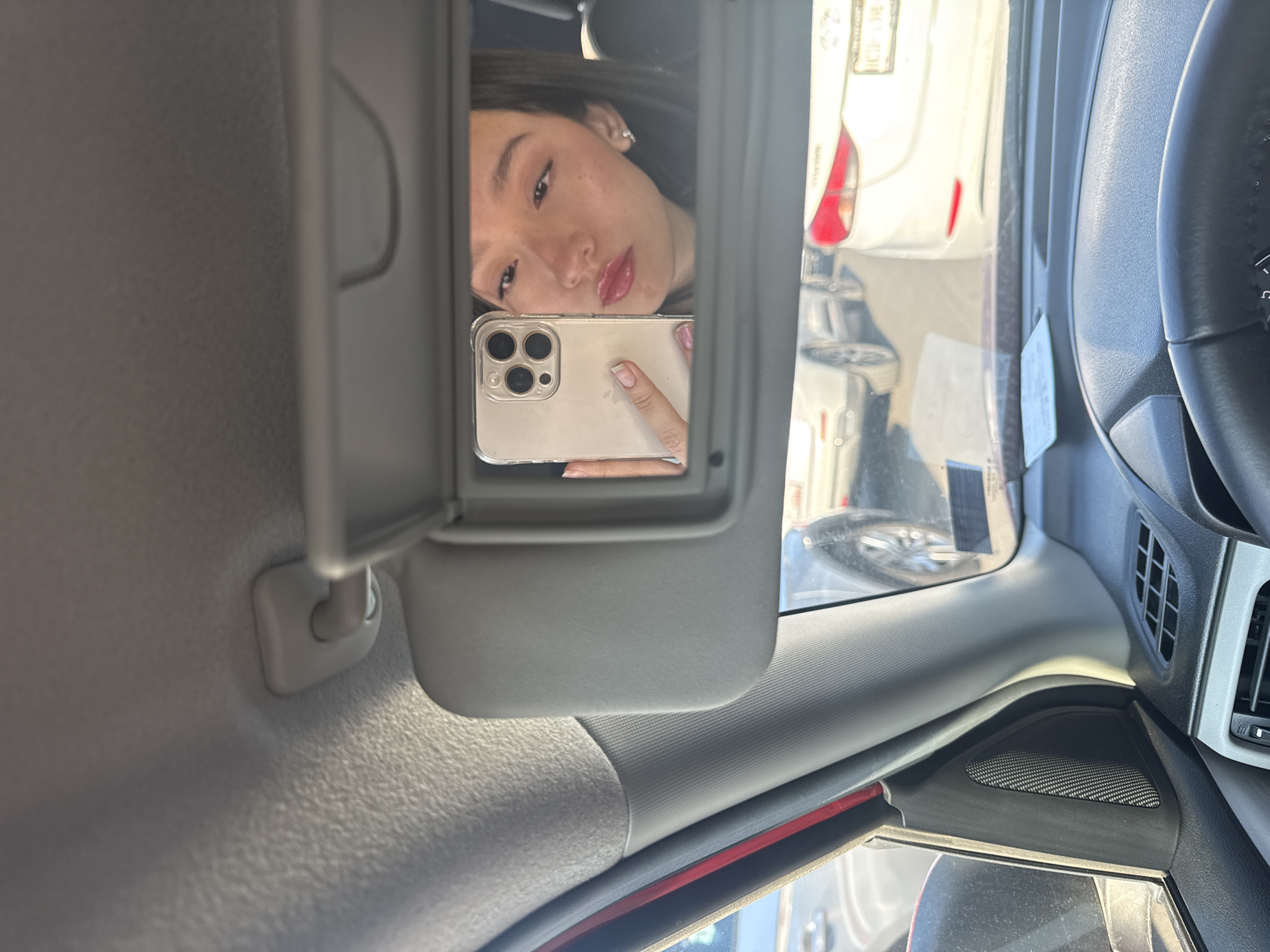 A woman is taking a selfie in the visor mirror of a vehicle. The vehicle appears to be parked in Puebla, Mexico, evidenced by a license plate visible through the windshield.