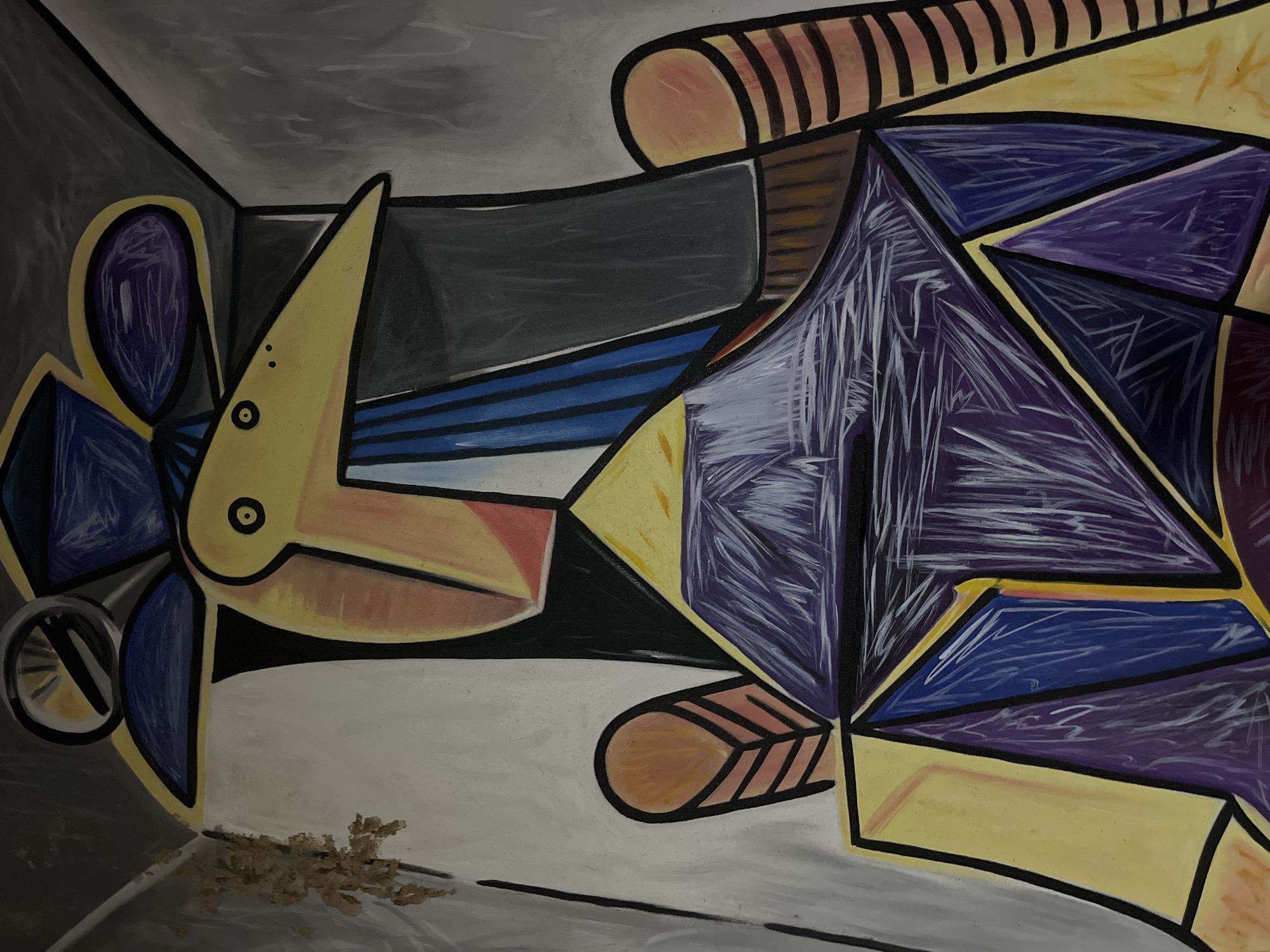 The image displays a painting in the Cubist style, featuring a portrait of a figure with geometric shapes and bold outlines. The figure is depicted wearing a hat and has a distinct facial structure with a long, beak-like nose, and two small circles for eyes. The dominant colors are yellow, purple, blue, and black, with accents of pink and white. The background appears to be a simplified interior space with grey walls. The painting exhibits textured brushstrokes, particularly in the purple areas of the figure's attire. There is a patch of discolored material on the upper left wall, possibly damage or debris. The painting is likely on canvas, given the visible texture.
This image was captured at Museum Pasifika, located in Kuta Selatan, Indonesia. Museum Pasifika is an art museum showcasing a collection of Pacific and Asian art. The painting itself is part of this collection.