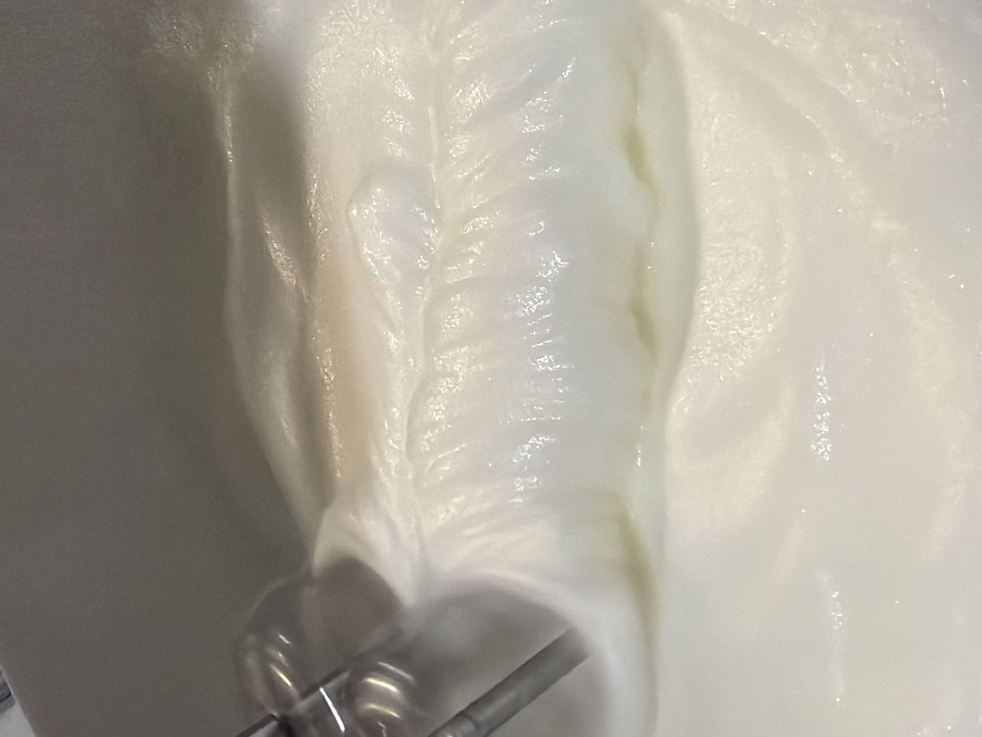 The image shows a close-up view of a white, viscous substance, possibly cream or batter, being mixed with a tool that has metallic components. The substance is swirling and folding over itself, indicating movement and mixing. The environment appears to be a mixing bowl or container. There are no identifiable people, actions, or interactions beyond the mixing process. The location in Sofia, Bulgaria is unknown.