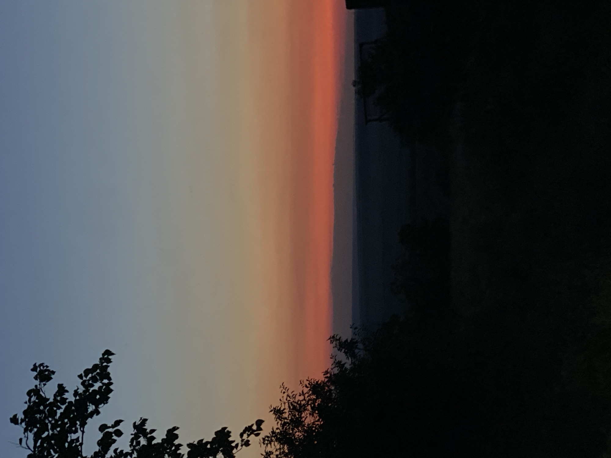 The image shows a landscape at dusk. The sky transitions from a deep blue at the top to shades of orange and red near the horizon. Silhouetted trees and foliage frame the scene from the left and right, with a dark, indistinct landscape visible in the middle ground. The location is specified as Cairaclia, Moldova. The image is a still photograph, depicting a natural environment with no human subjects or discernible activity. The overall impression is one of a peaceful, natural setting at twilight.
